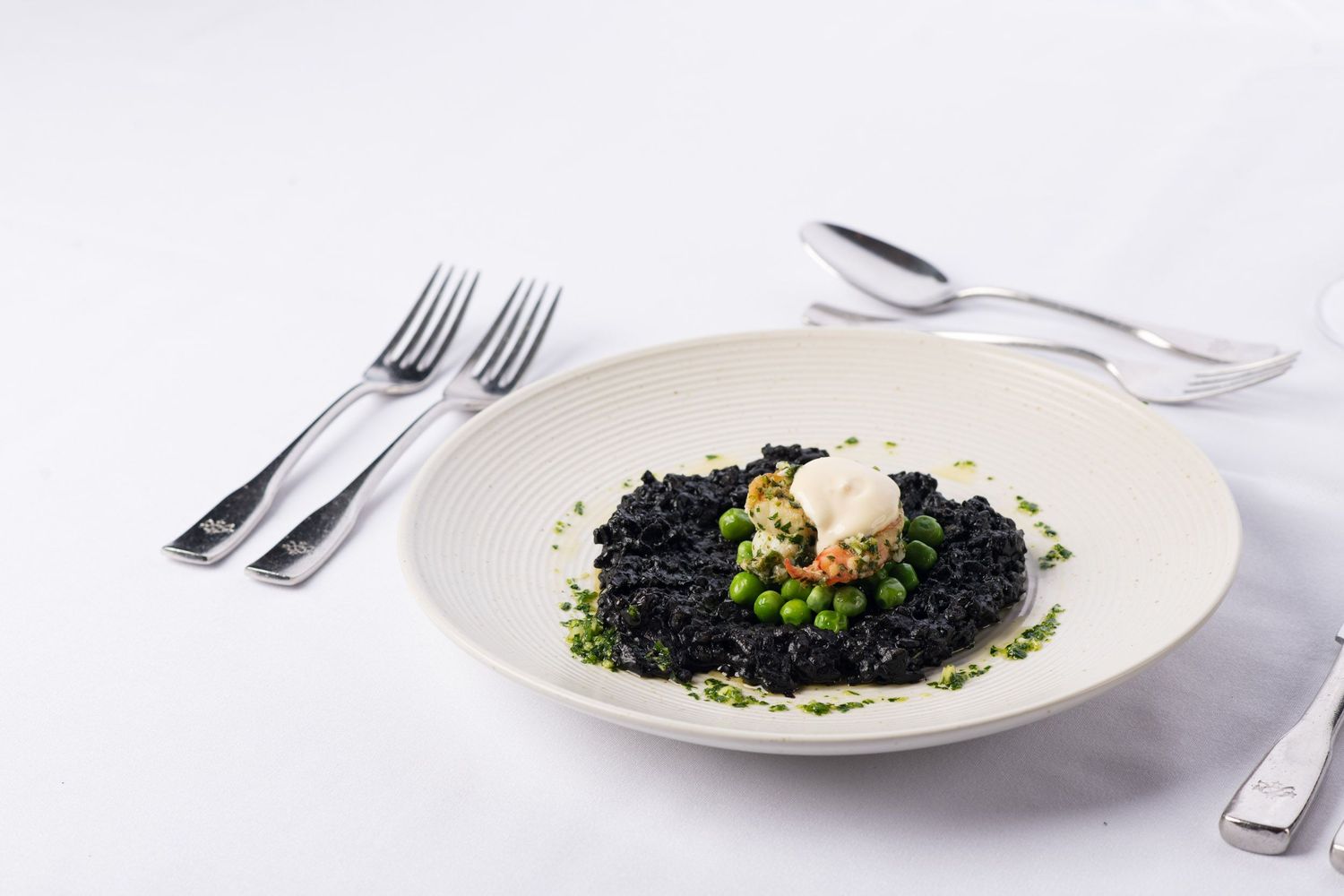 Gourmet black squid ink risotto with green peas and seafood garnish on a white plate.