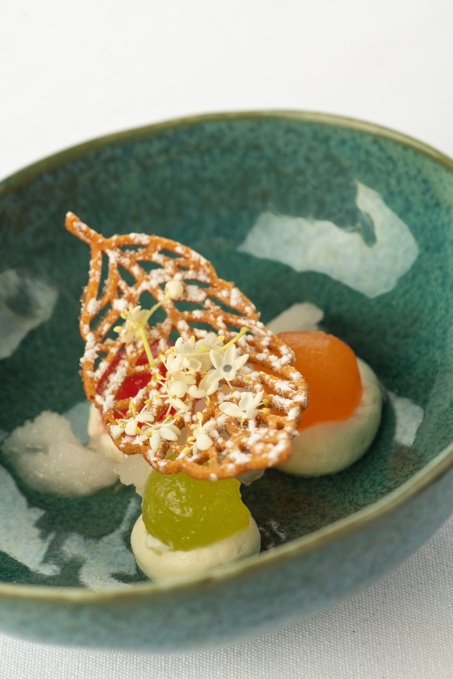 Artistic fine dining dessert in a green ceramic bowl with decorative lace tuile and fruit.