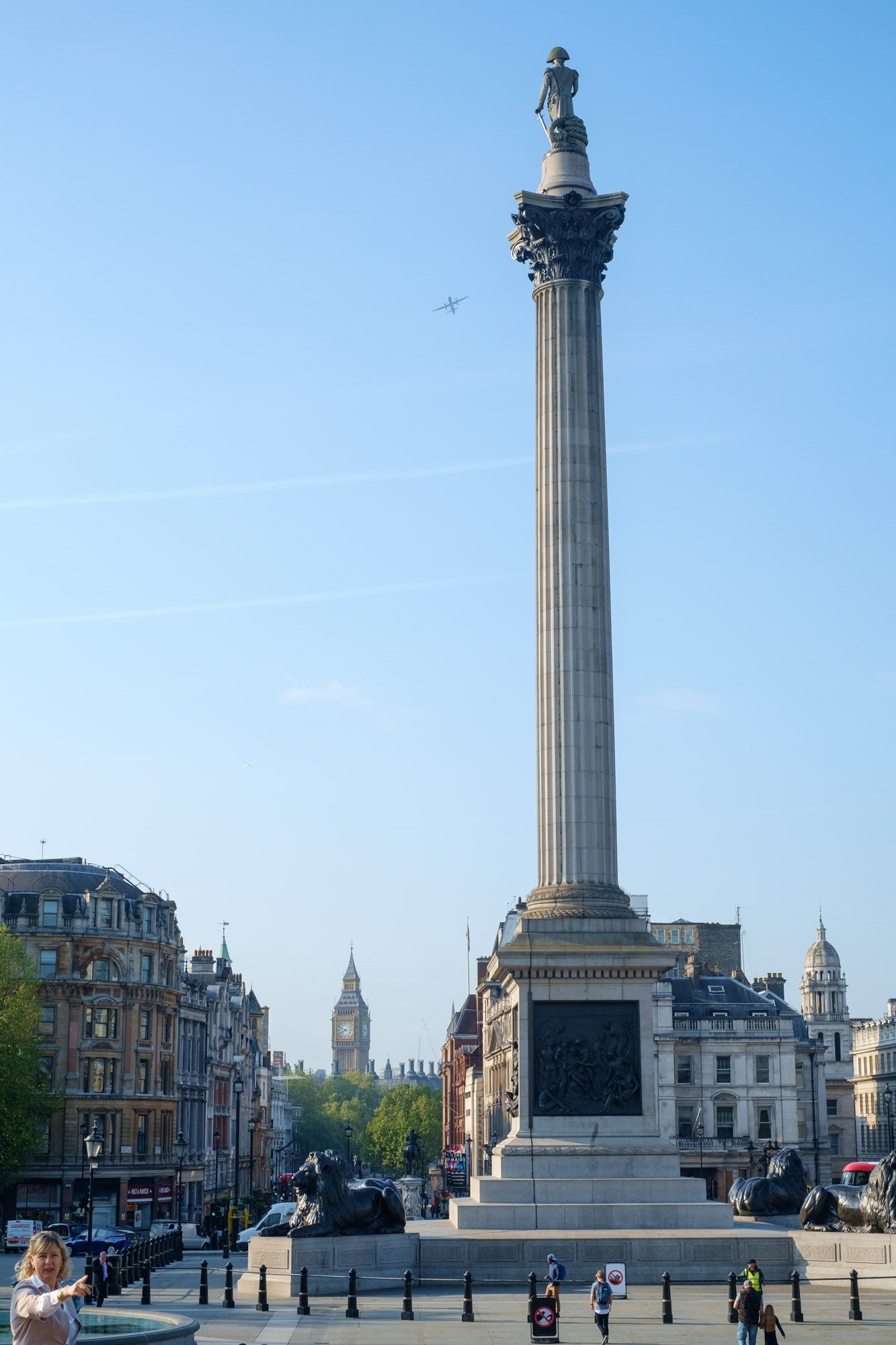 Nelson's Column at Trafalgar Square in London with Big Ben visible in the background under blue sky.