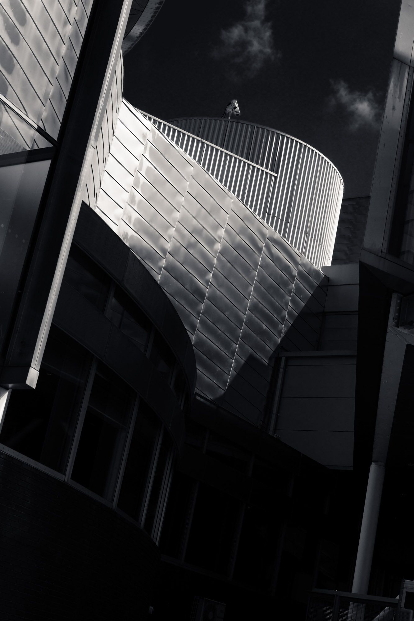 Low angle black and white shot of a curved metallic building exterior with spiral railing against dark sky.