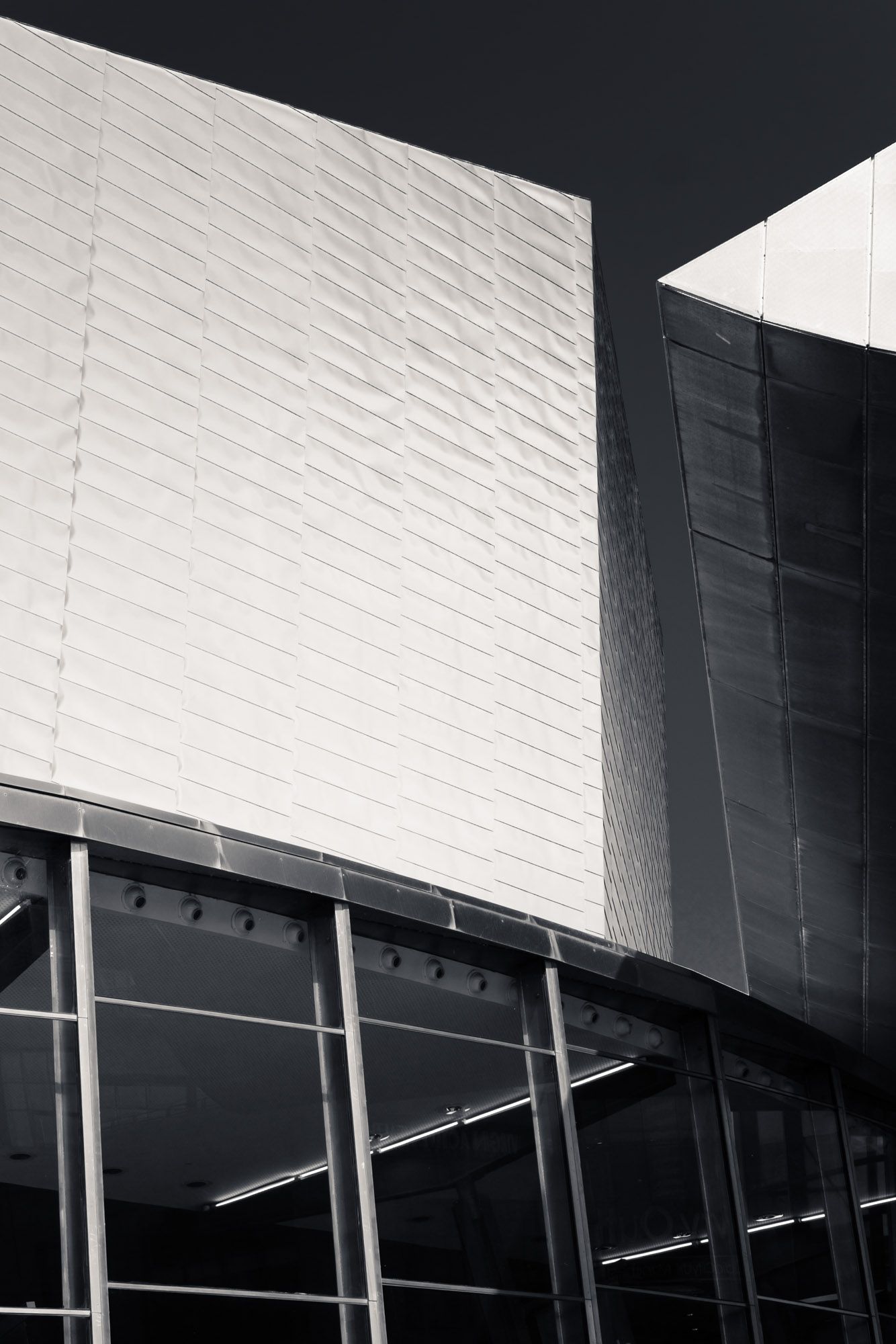 Black and white close-up of modern building exterior with textured white panels and curved glass facade.