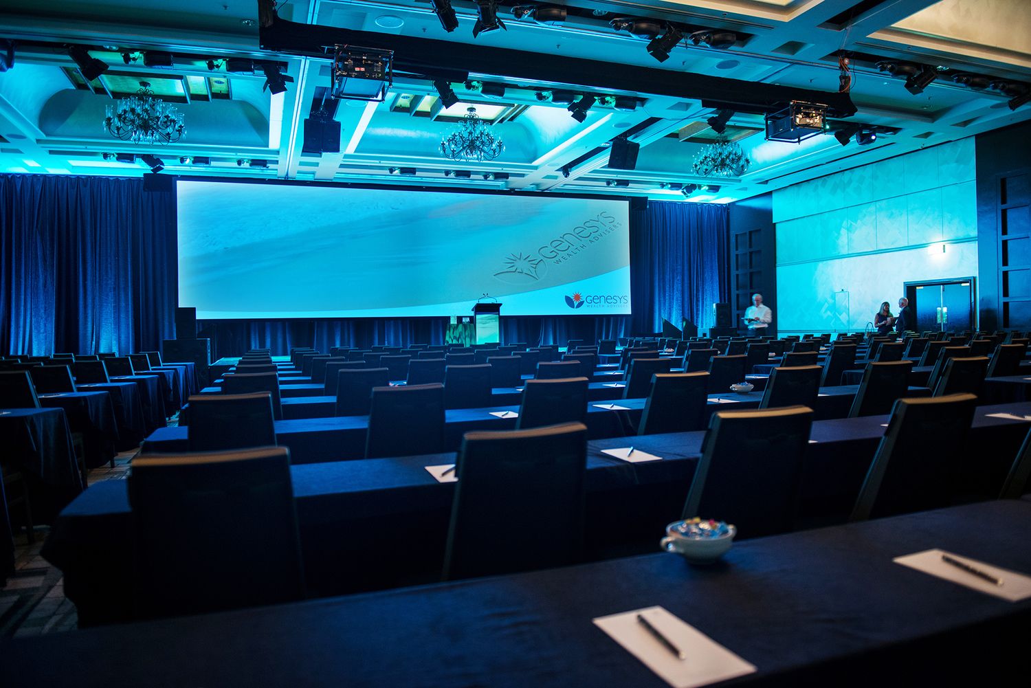 Empty conference hall with blue lighting, rows of chairs, and large presentation screens ready for event.