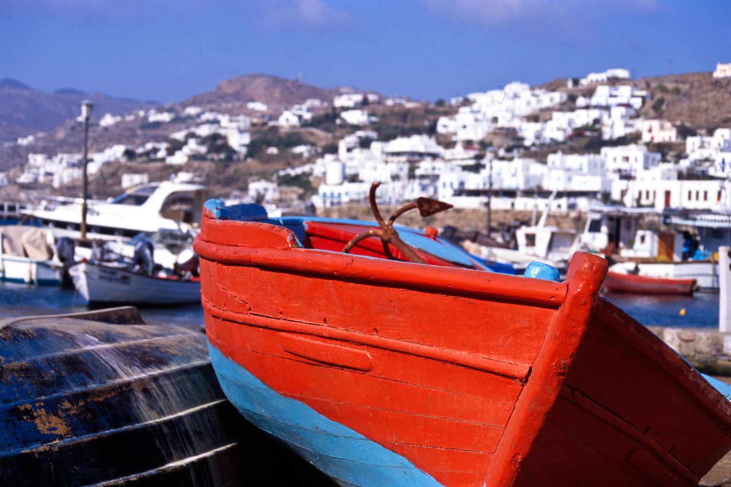 Colorful red and blue wooden fishing boat docked at a Greek island harbor with white buildings behind.
