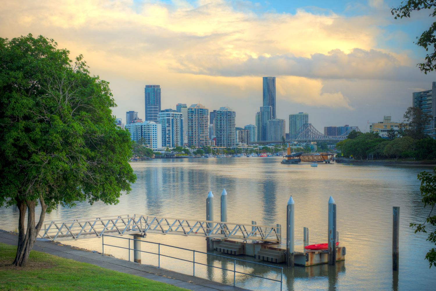 HDR cityscape of Brisbane river at sunset with a jetty and glowing skyline reflection.
