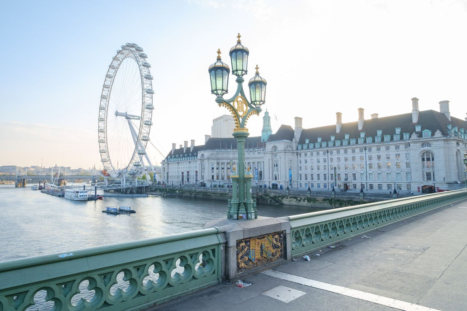London Eye Ferris wheel and County Hall viewed from Westminster Bridge with ornate green lampposts.