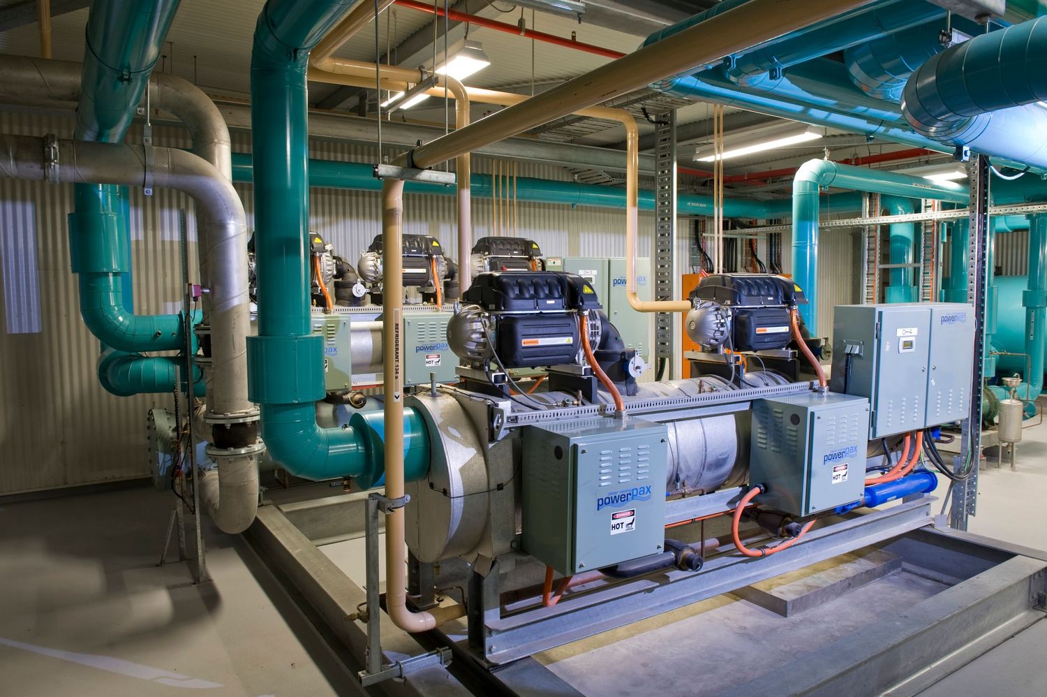 Industrial mechanical room with teal pipes, compressors, and HVAC equipment.