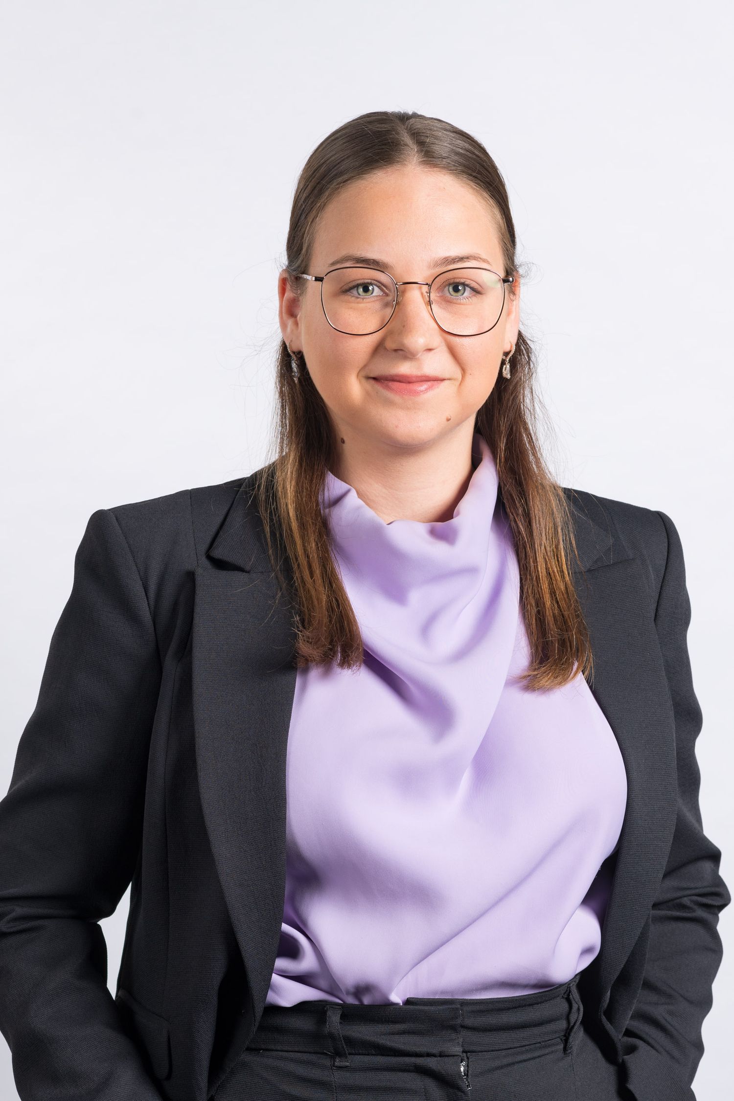 Young professional woman wearing glasses and lavender blouse under black blazer on white background.