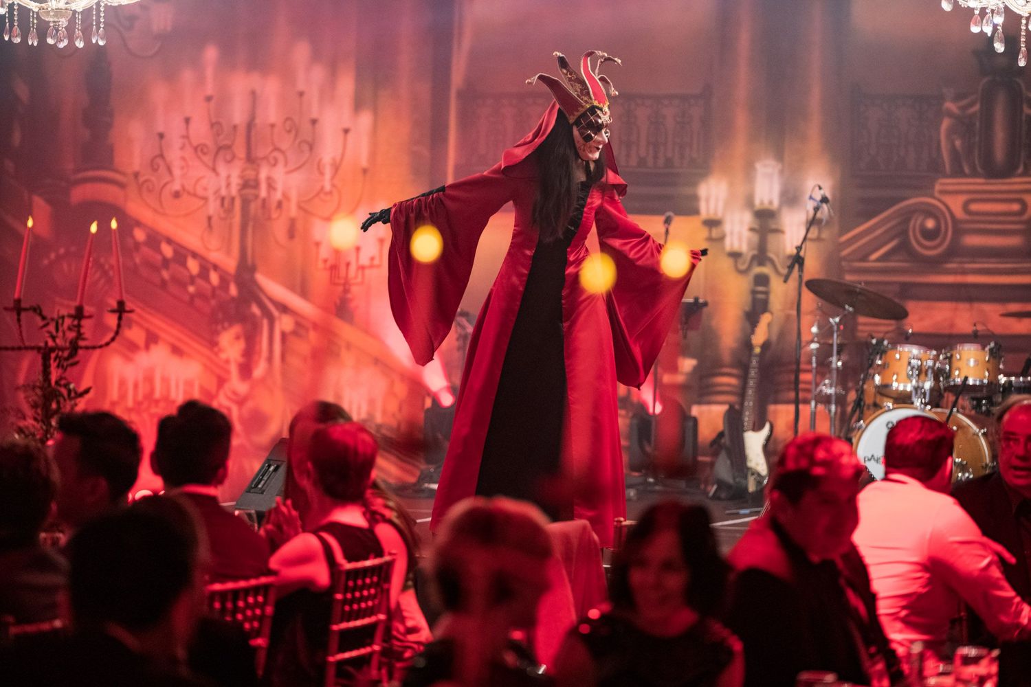 Dramatic red-costumed devil performer entertaining guests at a themed corporate event dinner with atmospheric lighting.
