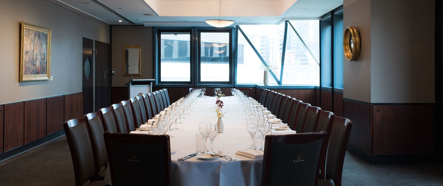 Formal private dining room with long conference table set with white linen and glassware.