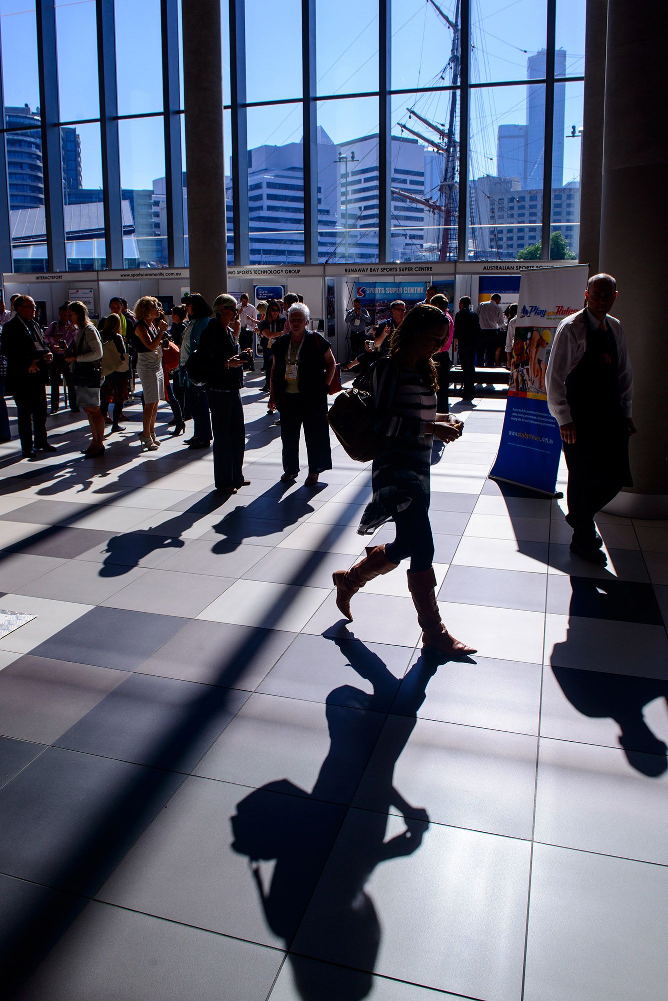 Silhouetted conference attendees walking through a sunlit modern convention center with city views.