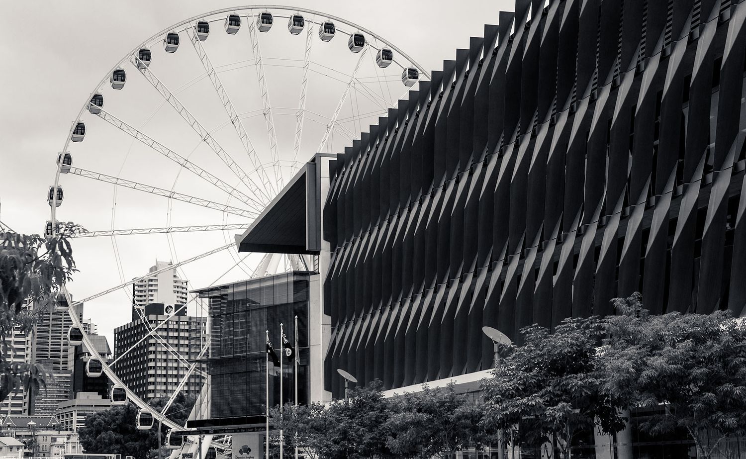 Black and white photo of a large Ferris wheel beside a modern angular building in the city.