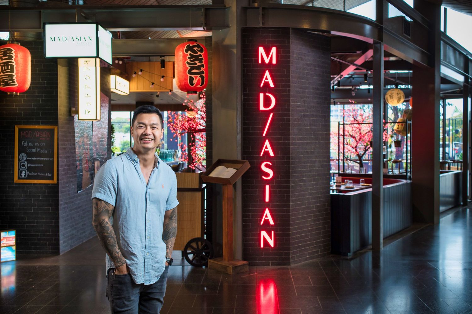 Man standing outside Mad Asian restaurant entrance with neon signage and Japanese lanterns.