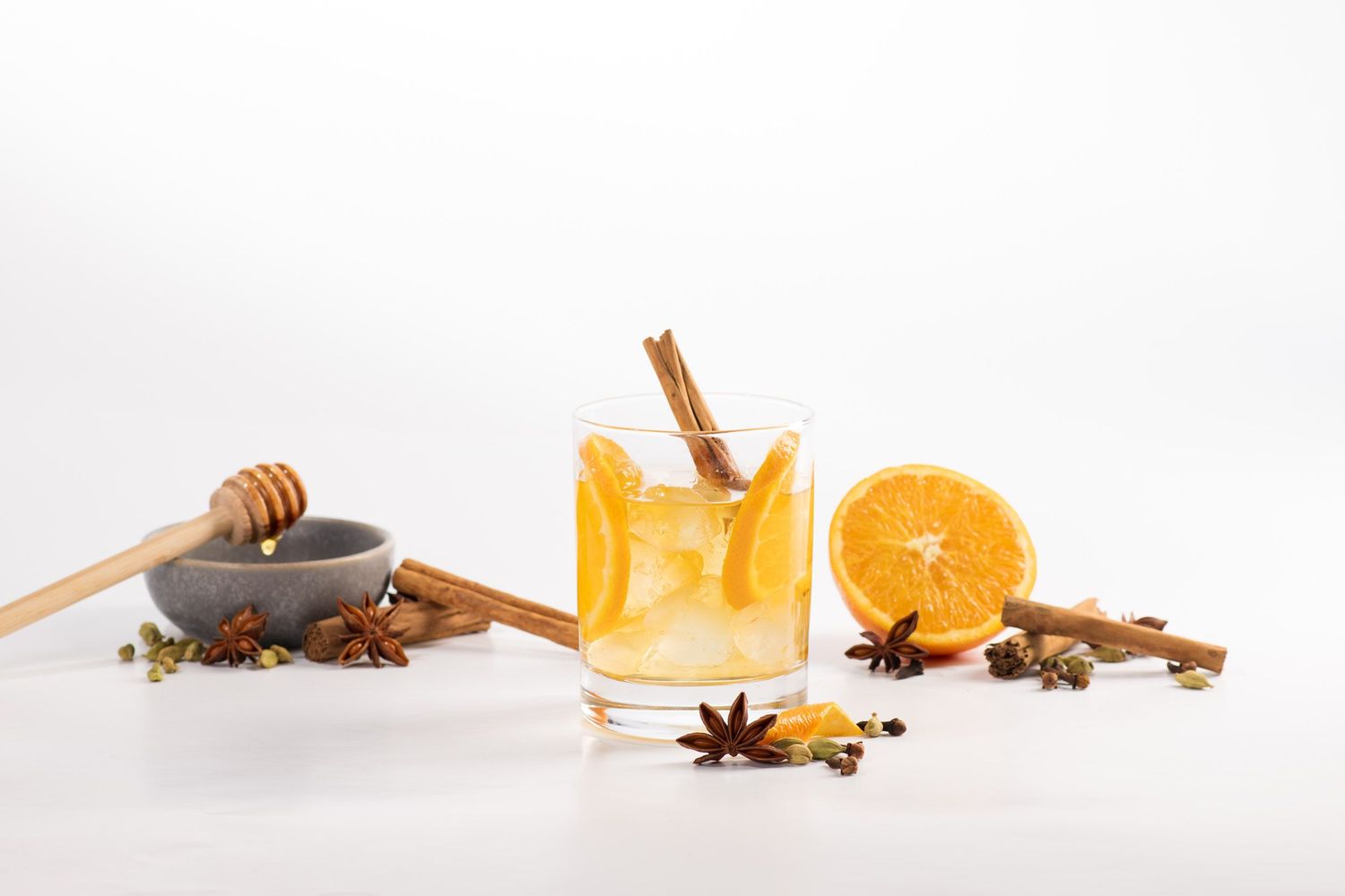 Orange and cinnamon cocktail with star anise and honey on white background.