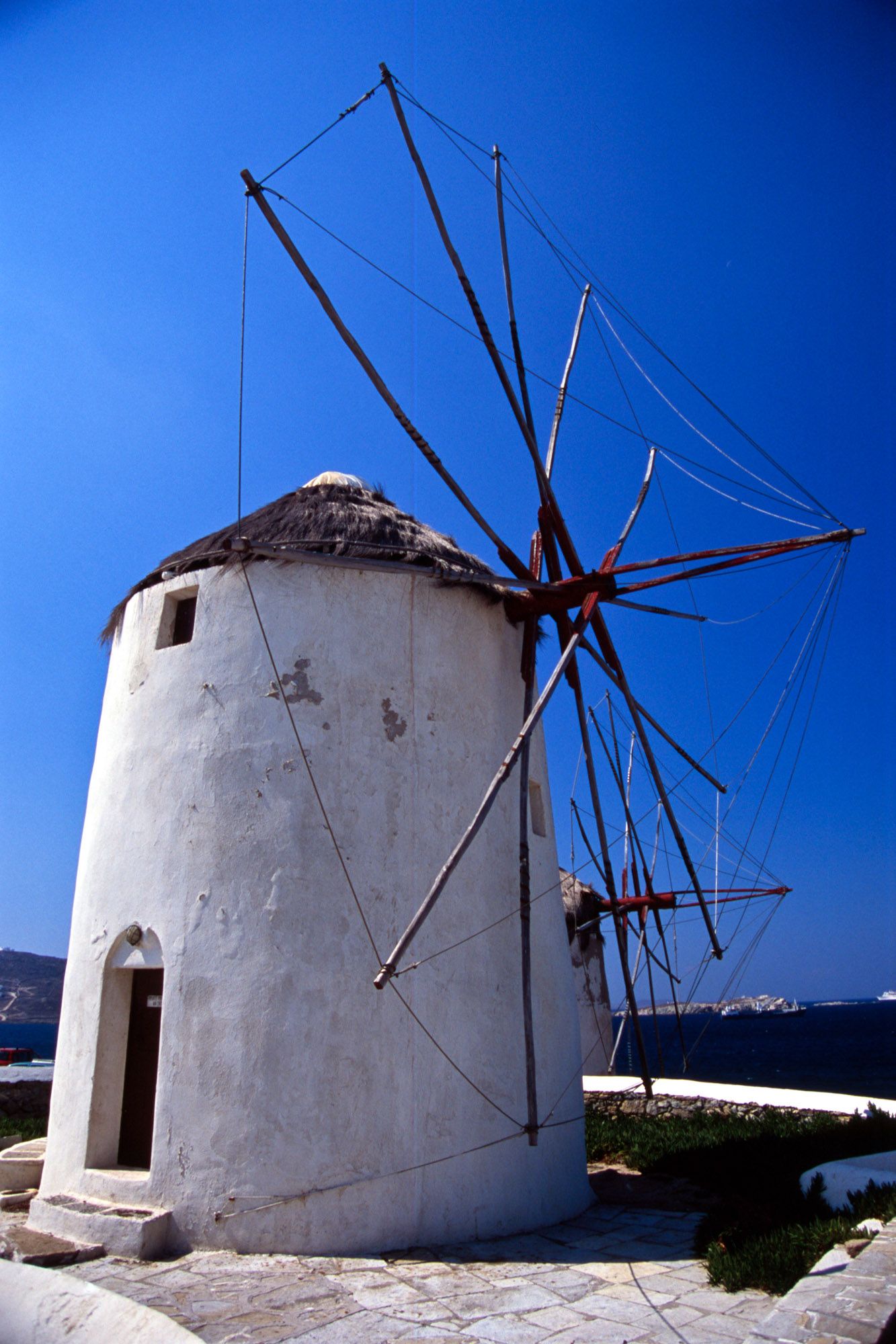 Traditional white Greek windmill with wooden sails on the island of Mykonos under blue sky.