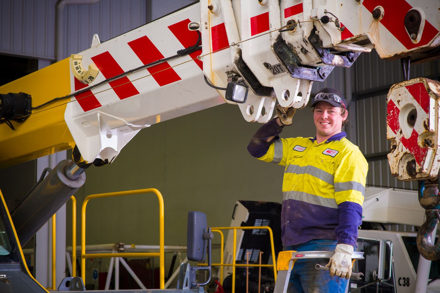 Worker in hi-vis yellow safety gear giving thumbs up beside heavy industrial machinery.