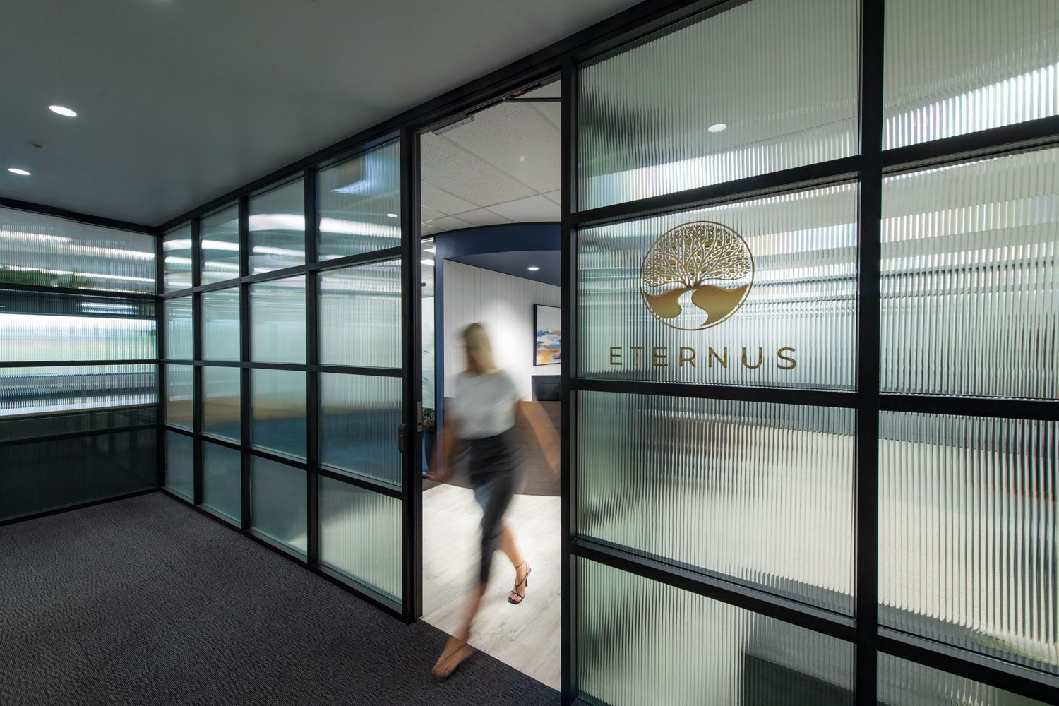 Blurred person walking through frosted glass office entrance with Eternus logo on modern door.
