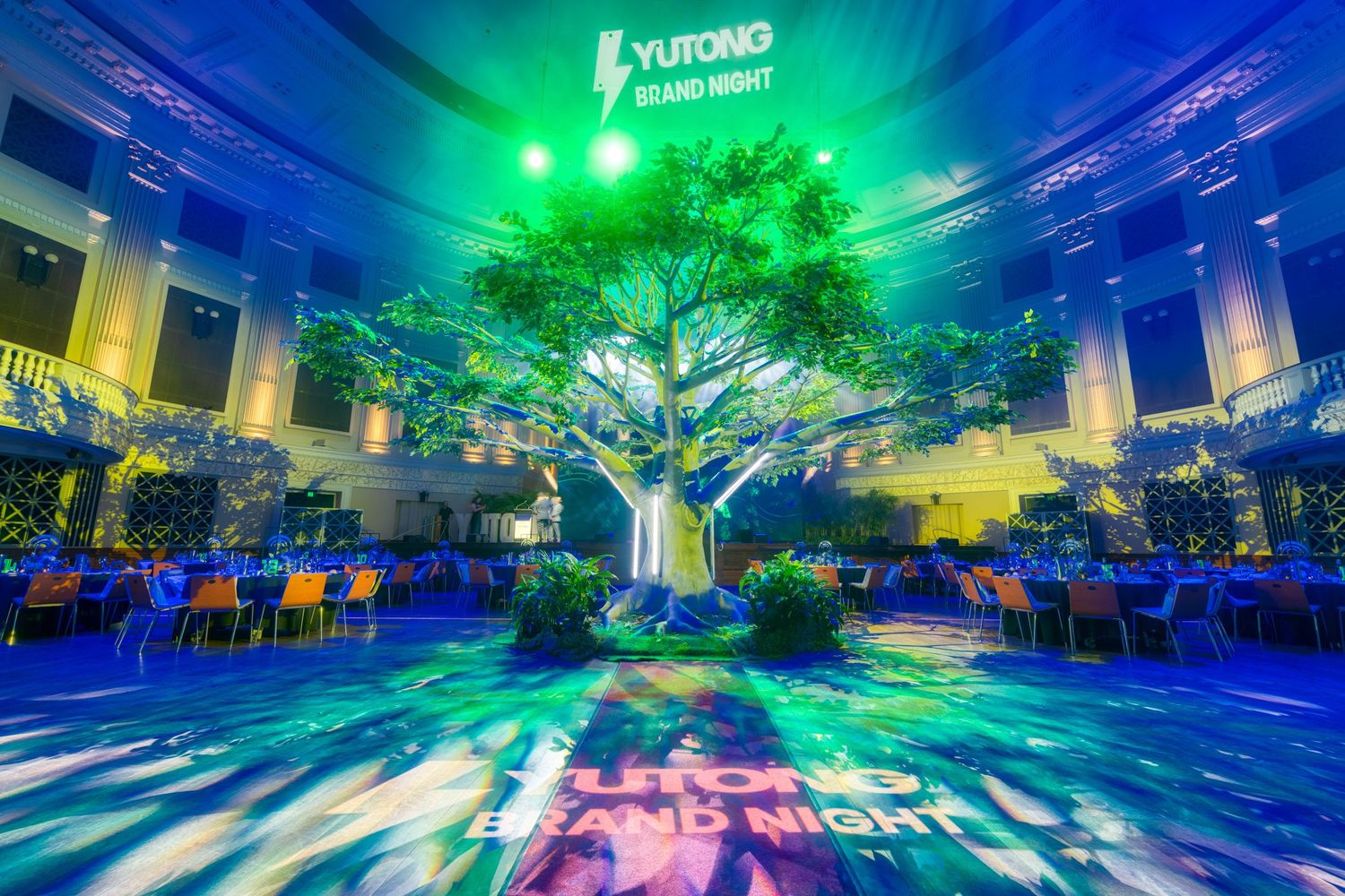 Yutong Brand Night event featuring a large illuminated tree centerpiece with vibrant green and blue projected lighting.