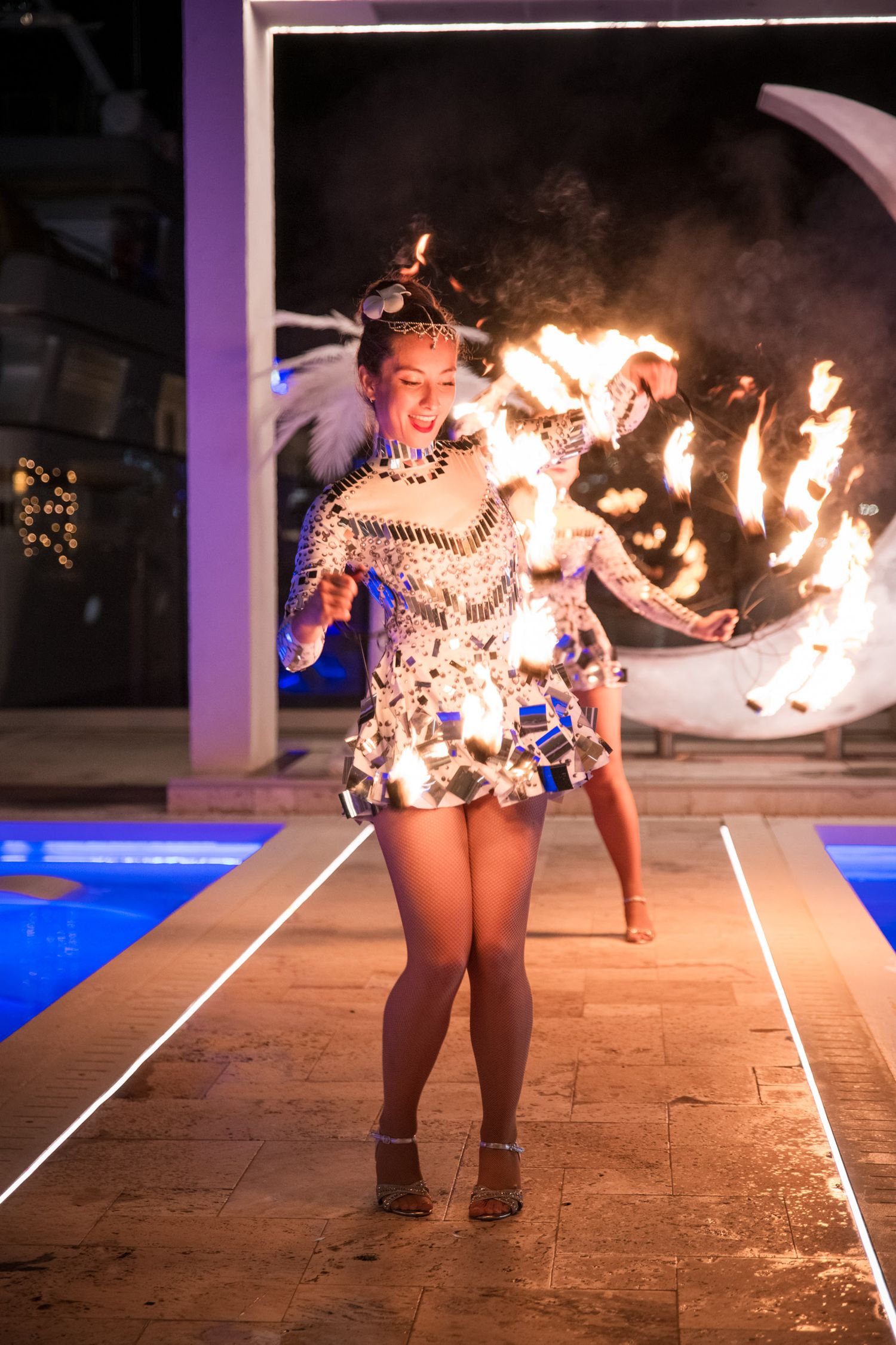 Female performer in sequined costume doing a fire dancing show on an illuminated runway at a night event.