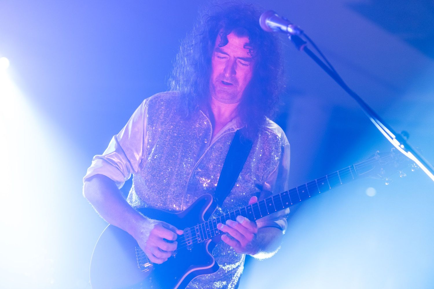 Guitarist with curly hair performing on stage under dramatic blue spotlight at live concert.