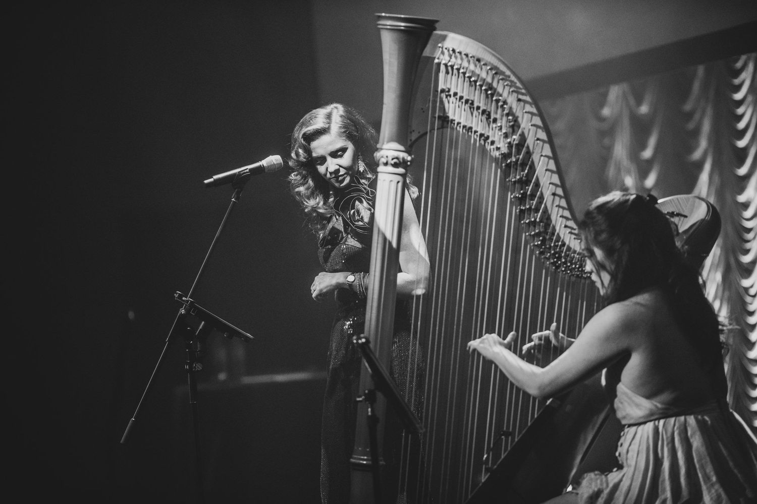 Black and white photo of two women performing on stage with a harp and microphone.