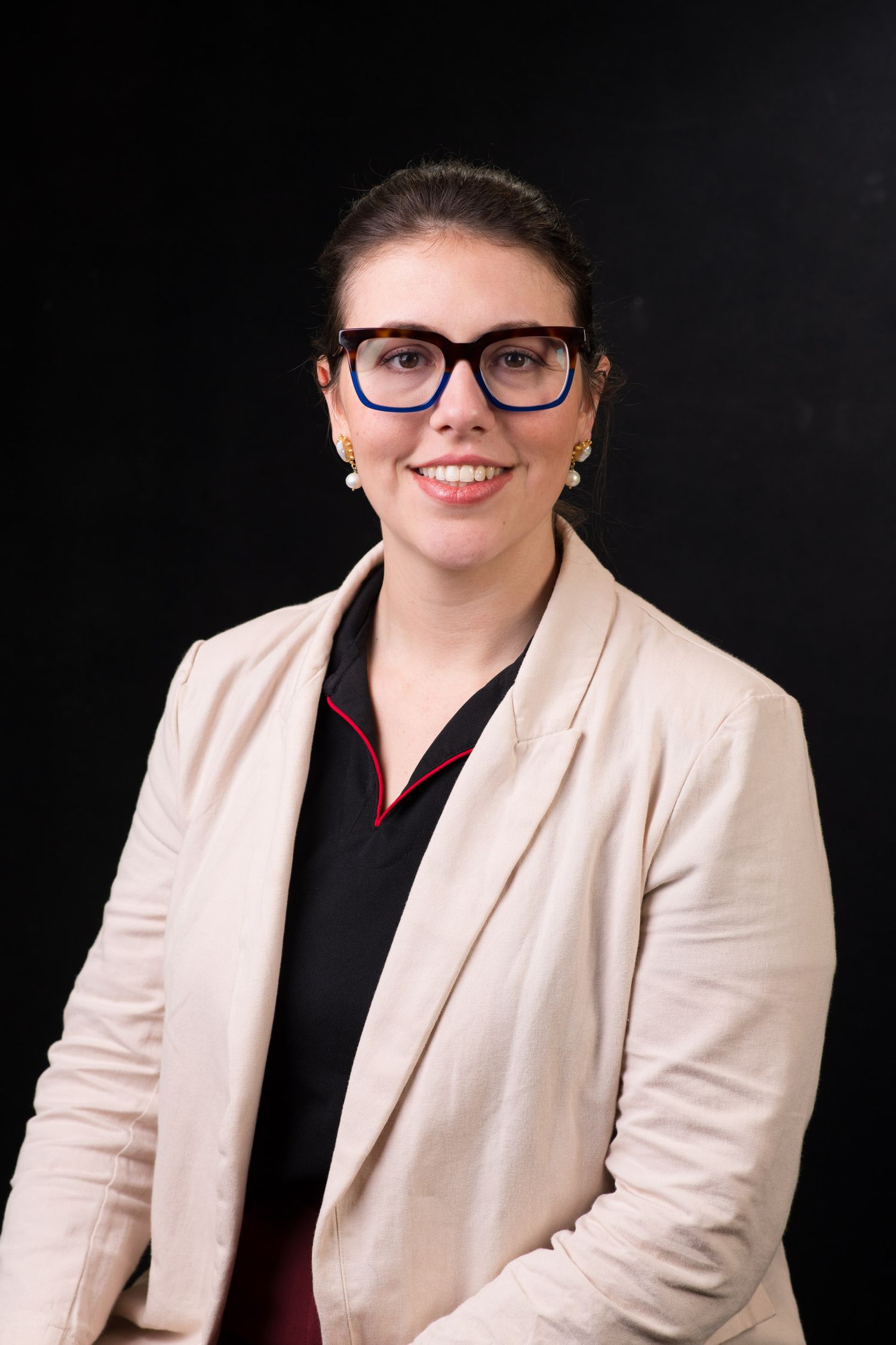 Smiling woman wearing glasses and a beige blazer poses for a professional portrait.