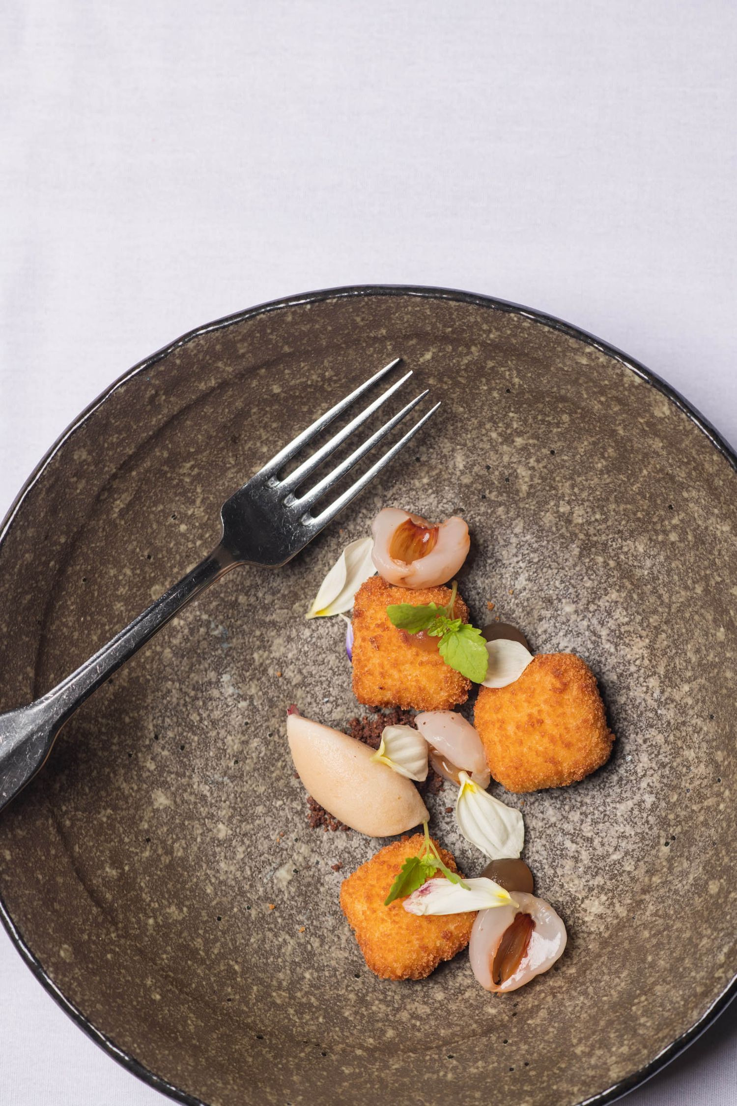 Golden fried croquettes with pickled onions and fresh herbs on a rustic dark ceramic plate with fork.