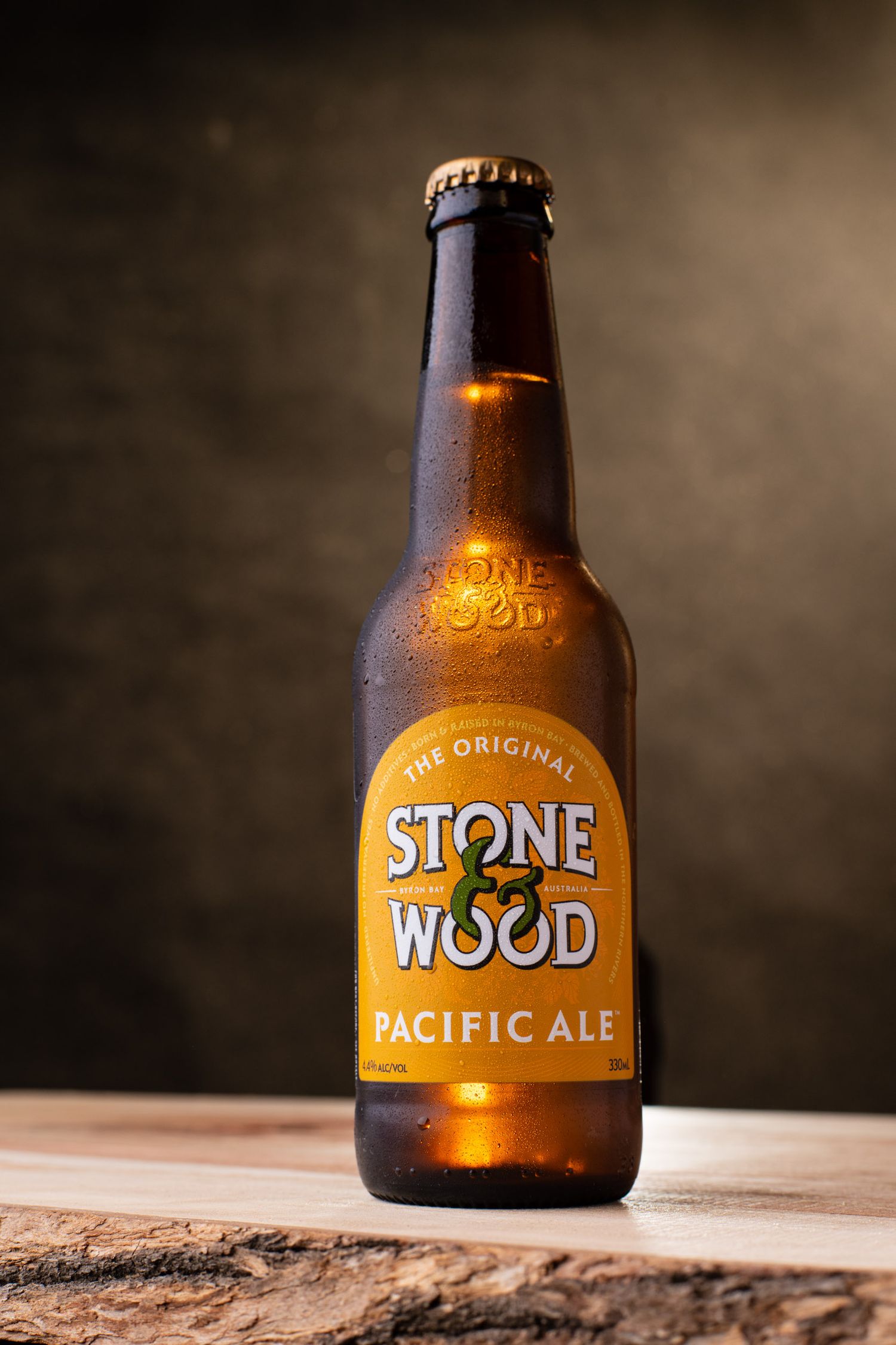 Stone & Wood Pacific Ale craft beer bottle on rustic wooden surface with dark background.