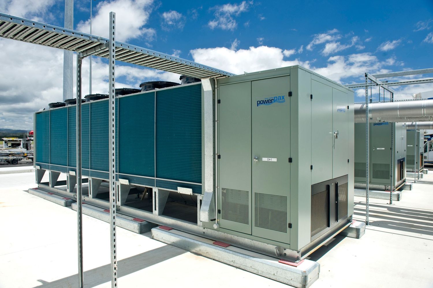 Commercial air-cooled chiller unit installed on rooftop under blue sky with clouds.