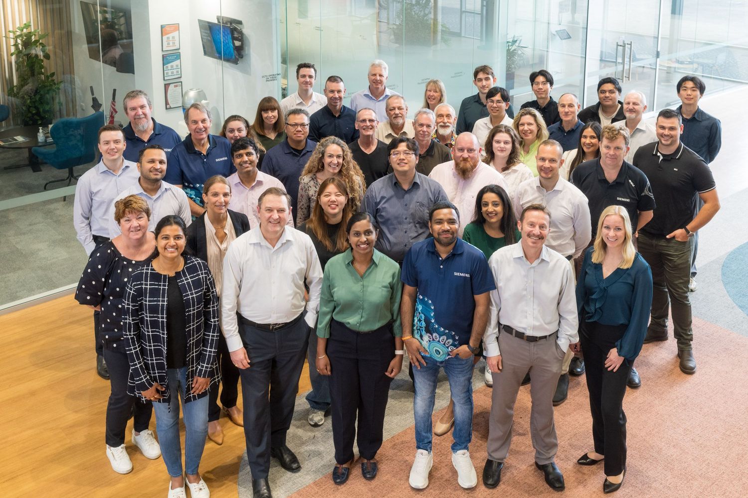 Large diverse corporate team posing together for a group photo in a modern office lobby.