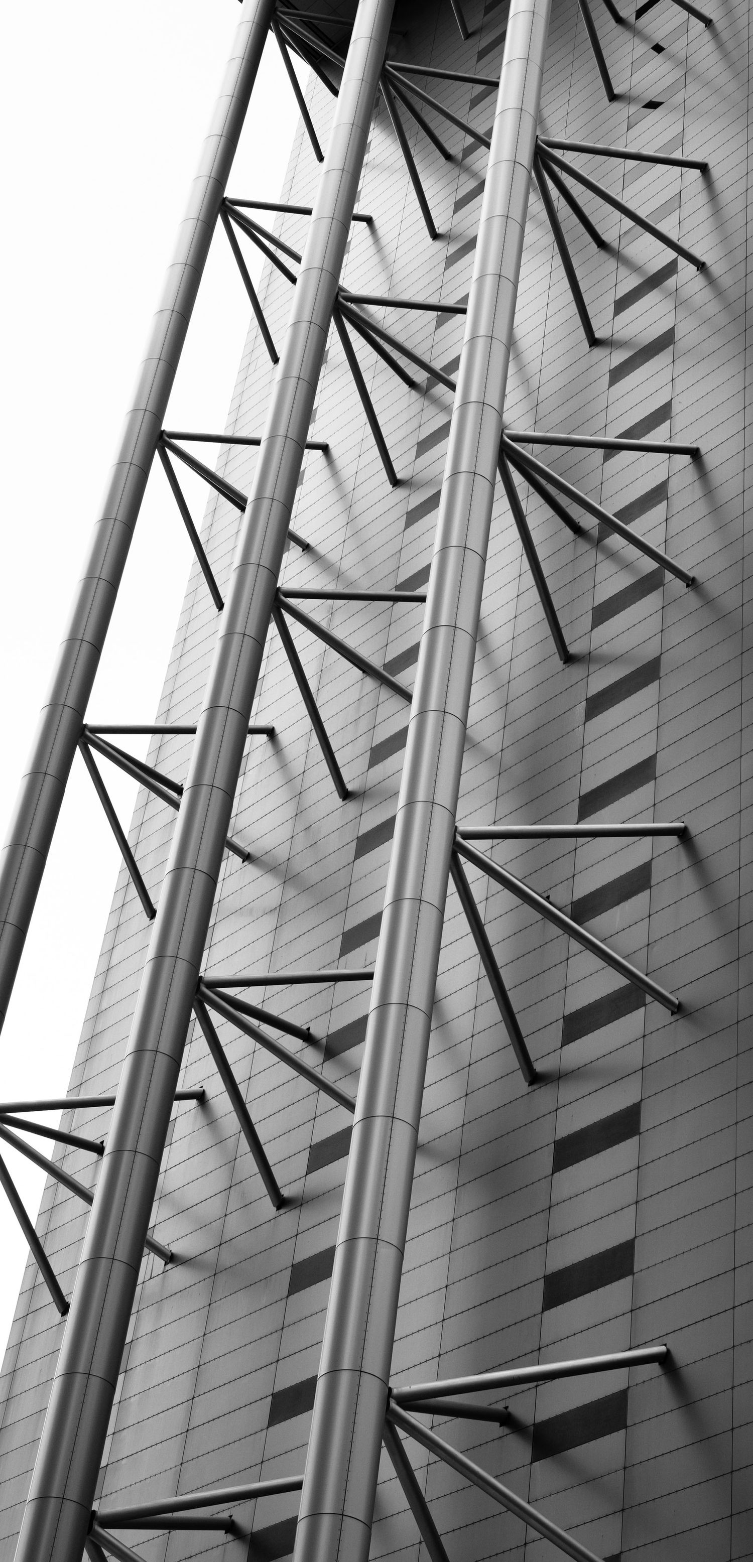 Black and white low-angle view of a skyscraper with dramatic angular steel structural elements.