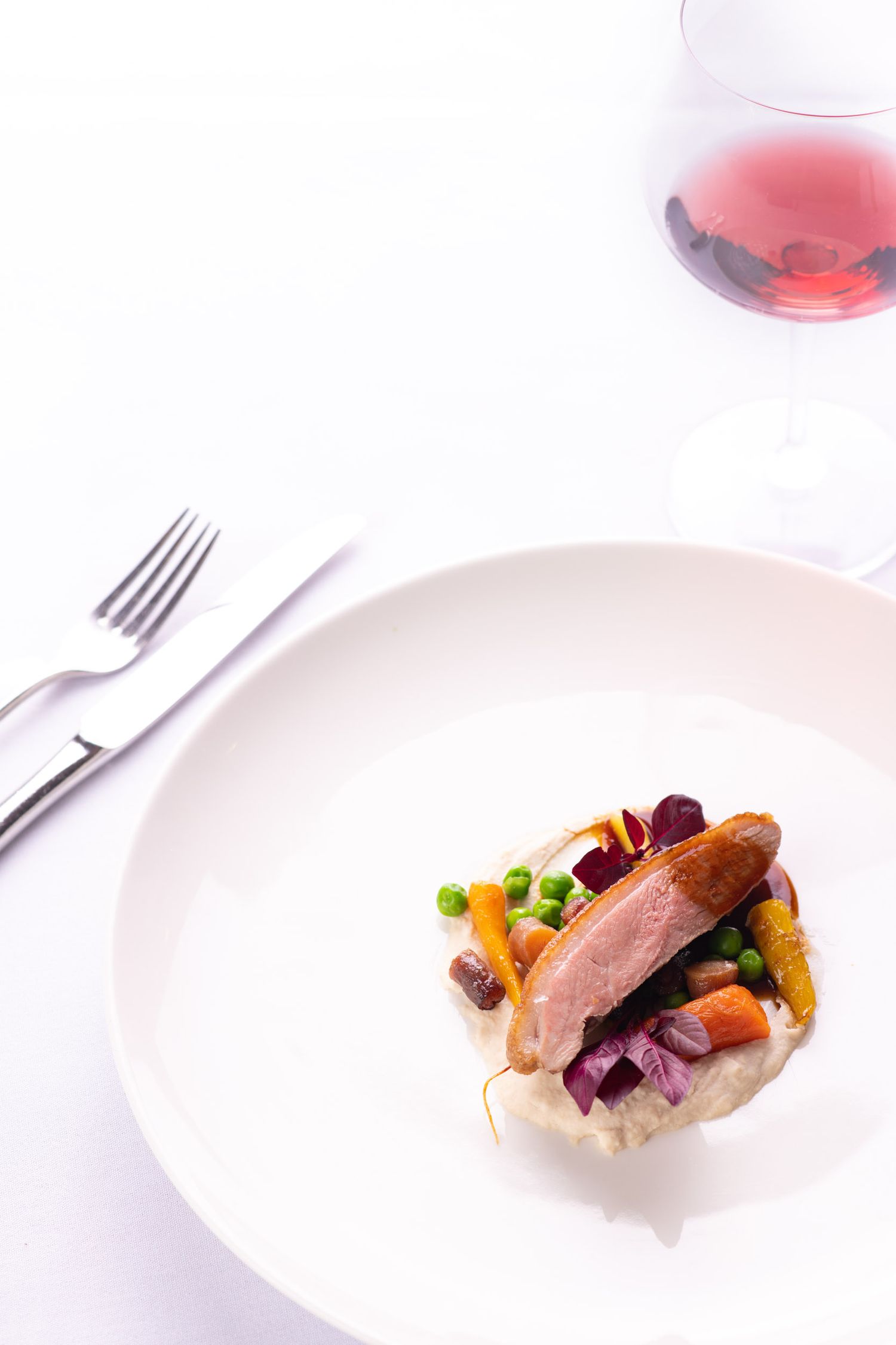 Fine dining duck breast with colorful vegetables on creamy mash, served with a glass of rose wine.