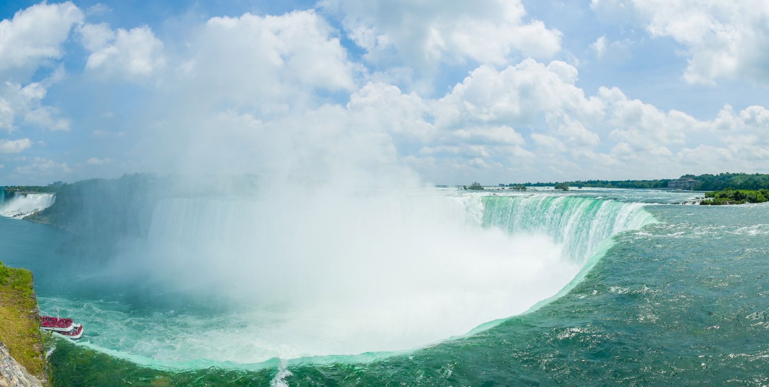 Panoramic view of Niagara Falls Horseshoe Falls with mist rising and tourist boat in turquoise water.