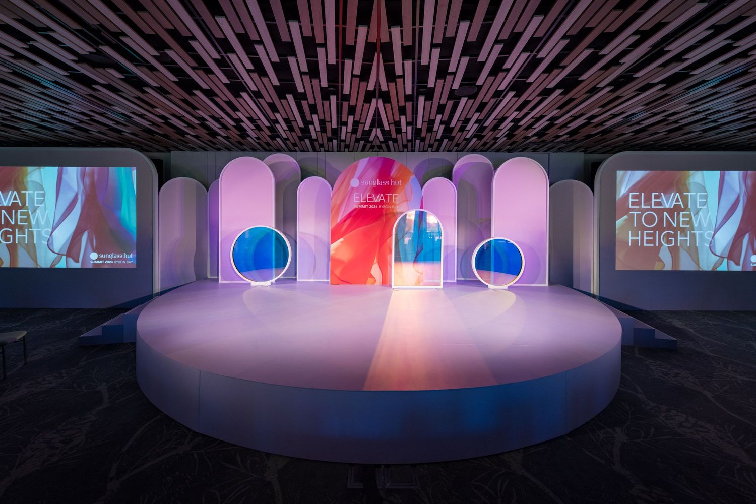 Modern event stage with arched white panels, circular windows, and colorful LED displays reading Elevate.