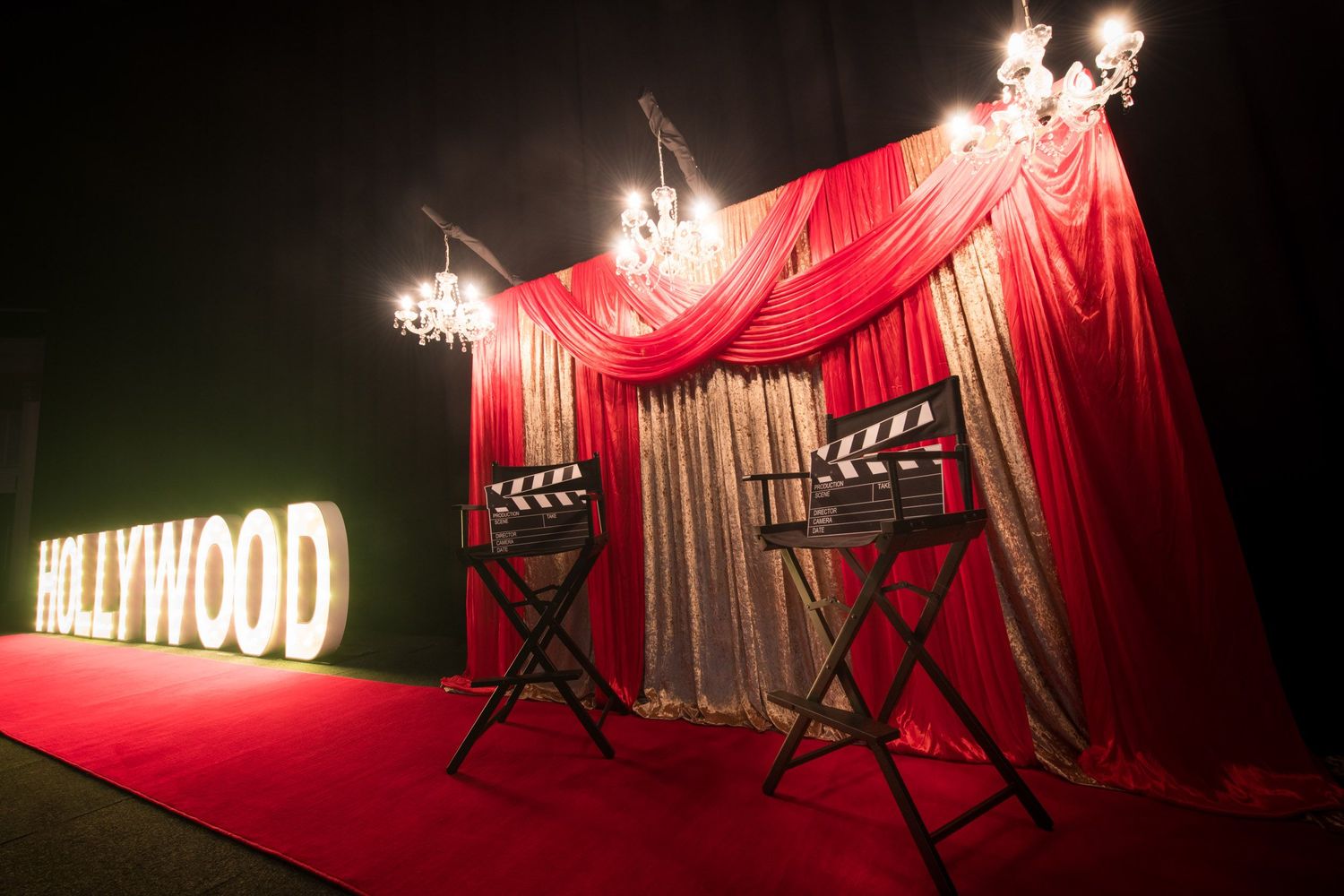 Hollywood-themed event setup with red carpet, director chairs, chandelier, and illuminated HOLLYWOOD marquee letters.