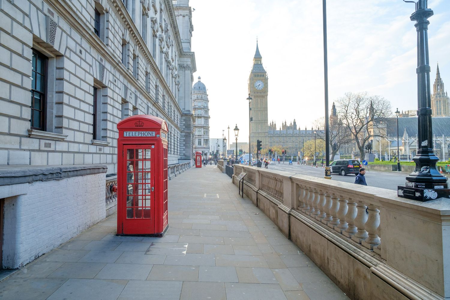 Iconic red British telephone box on Westminster Bridge Street with Big Ben and Parliament in background.