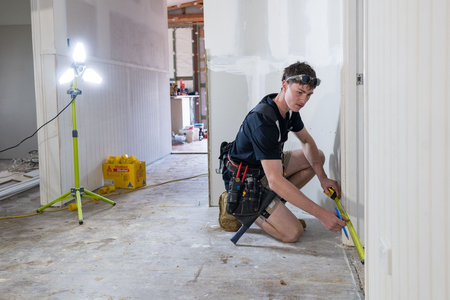 Young male tradesperson measures wall with tape measure during home renovation construction project.