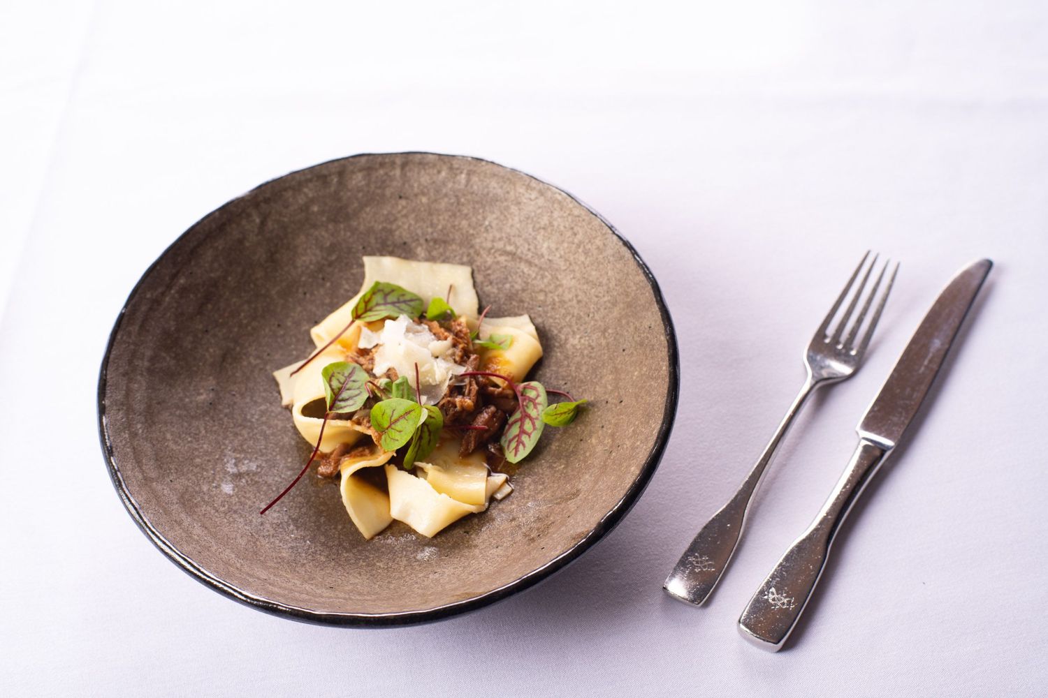Rustic bowl of pappardelle pasta with mushrooms, fresh herbs, and parmesan on a linen tablecloth.
