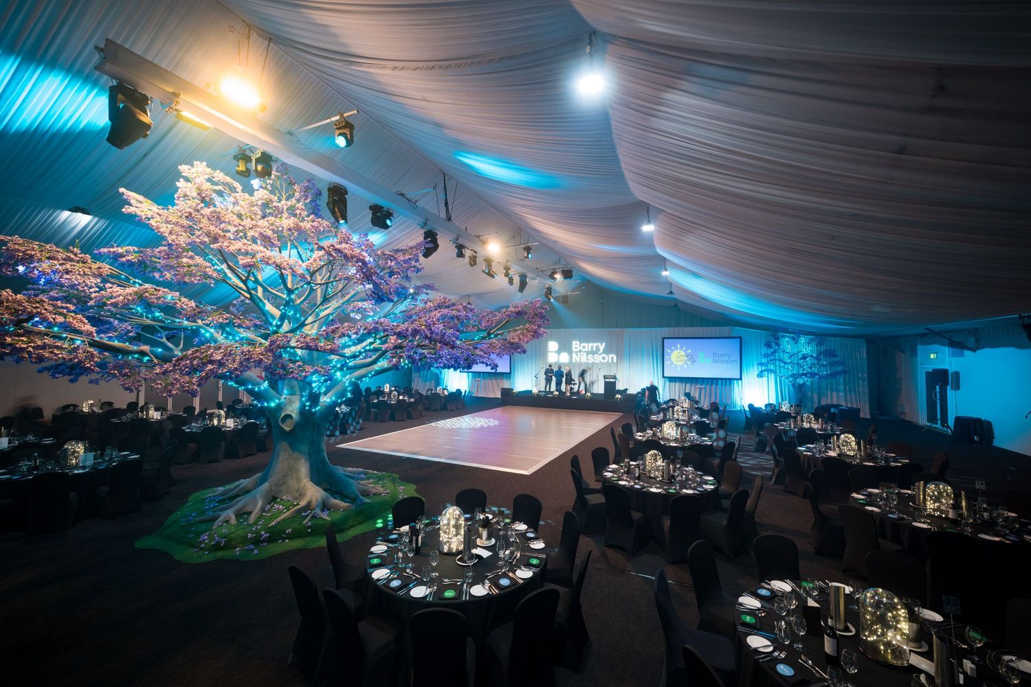 Enchanting event venue with illuminated decorative tree centerpiece and elegant black table settings.