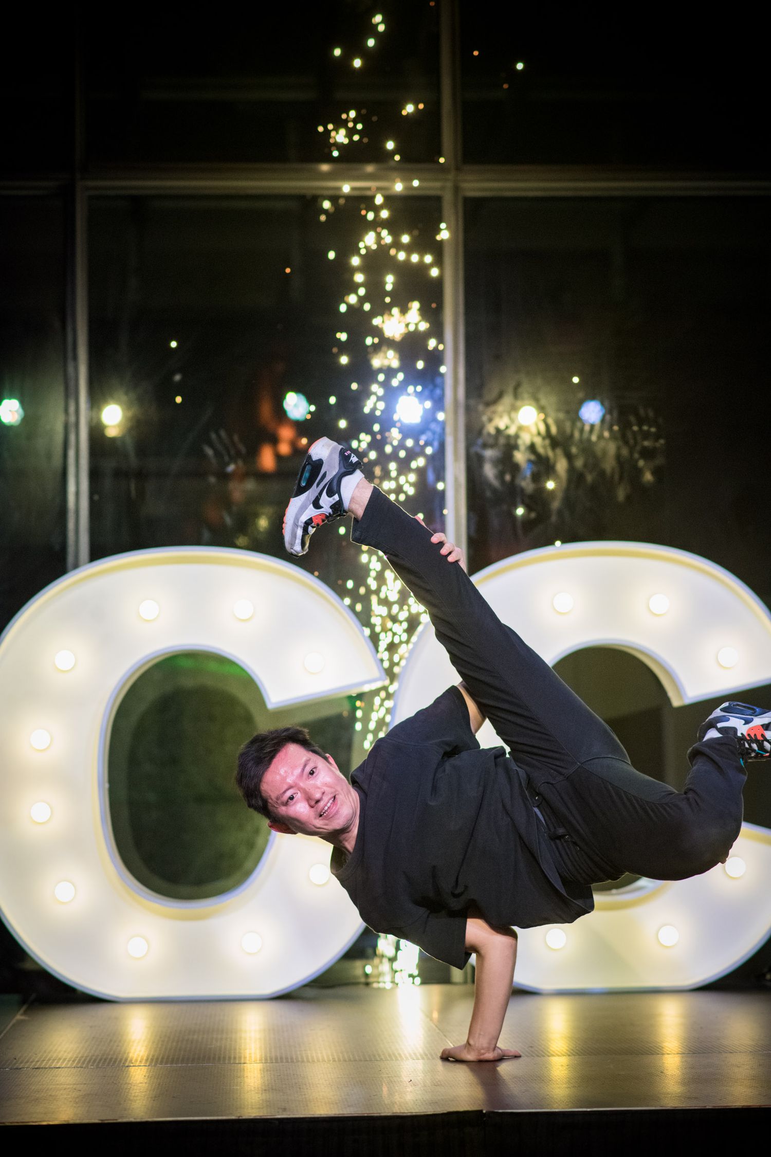 Breakdancer performing impressive one-handed freeze move in front of illuminated CC letters.