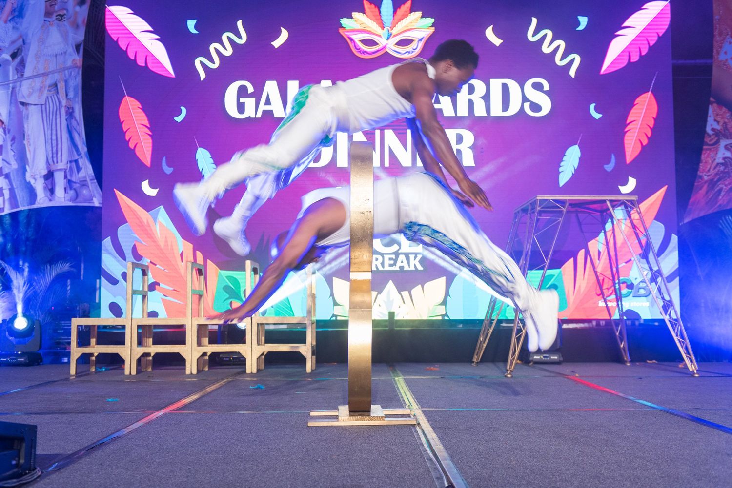 Acrobat performing limbo pole dance at Gala Awards Dinner event on colorful stage.