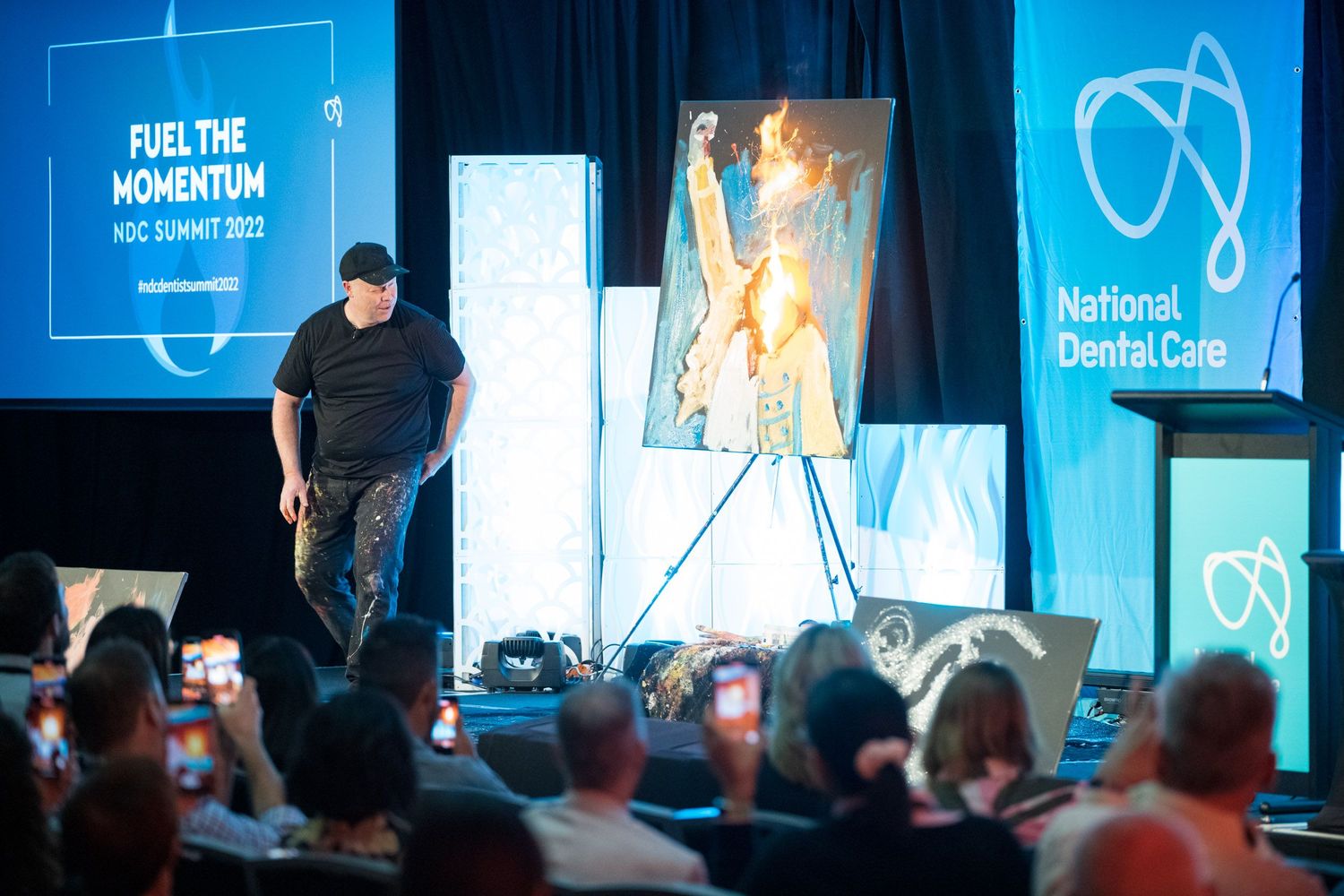Speaker presents artwork on stage at National Dental Care NDC Summit 2022 Fuel The Momentum conference event.