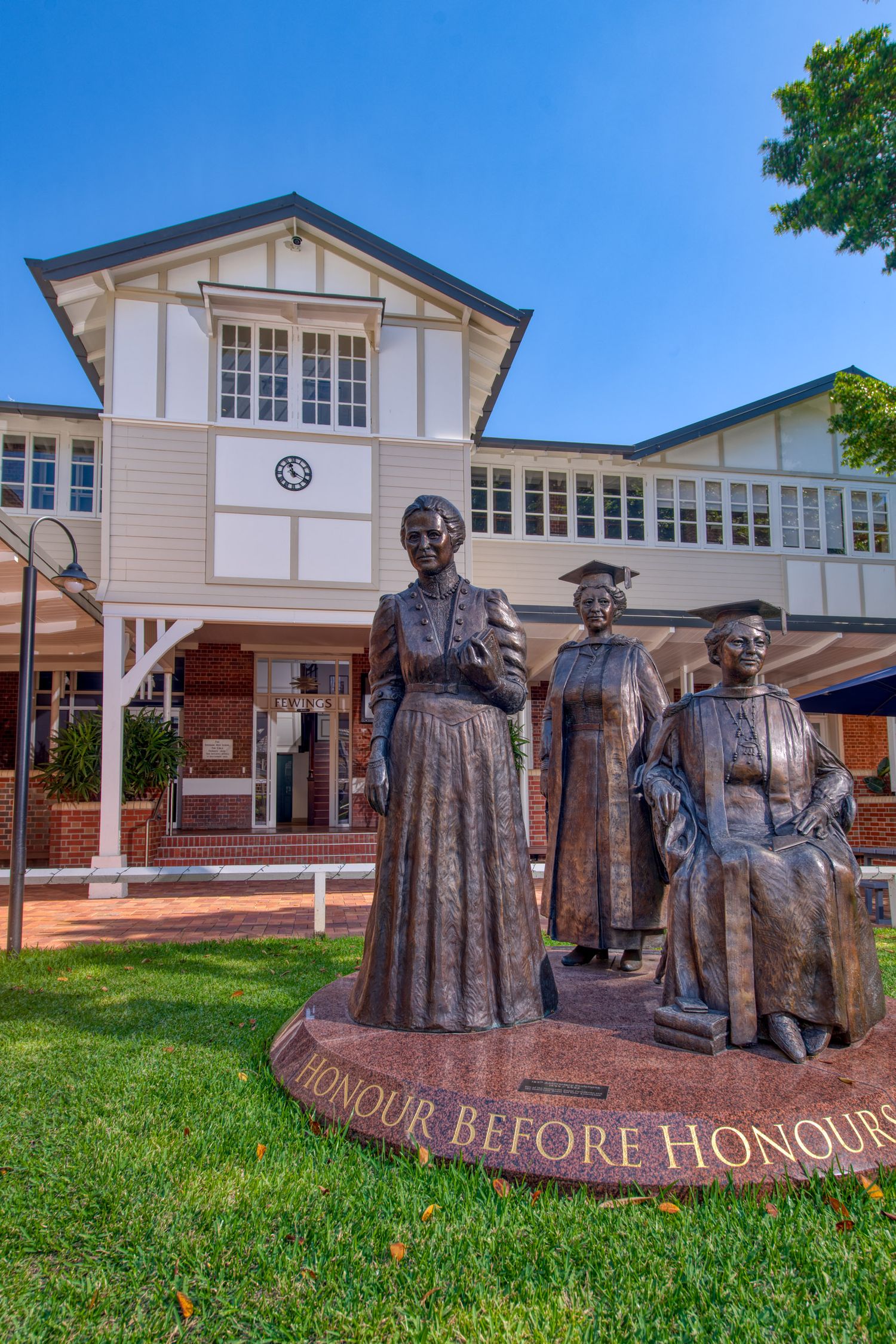 Bronze sculpture of three women with Honour Before Honours inscription outside heritage Queensland school building.