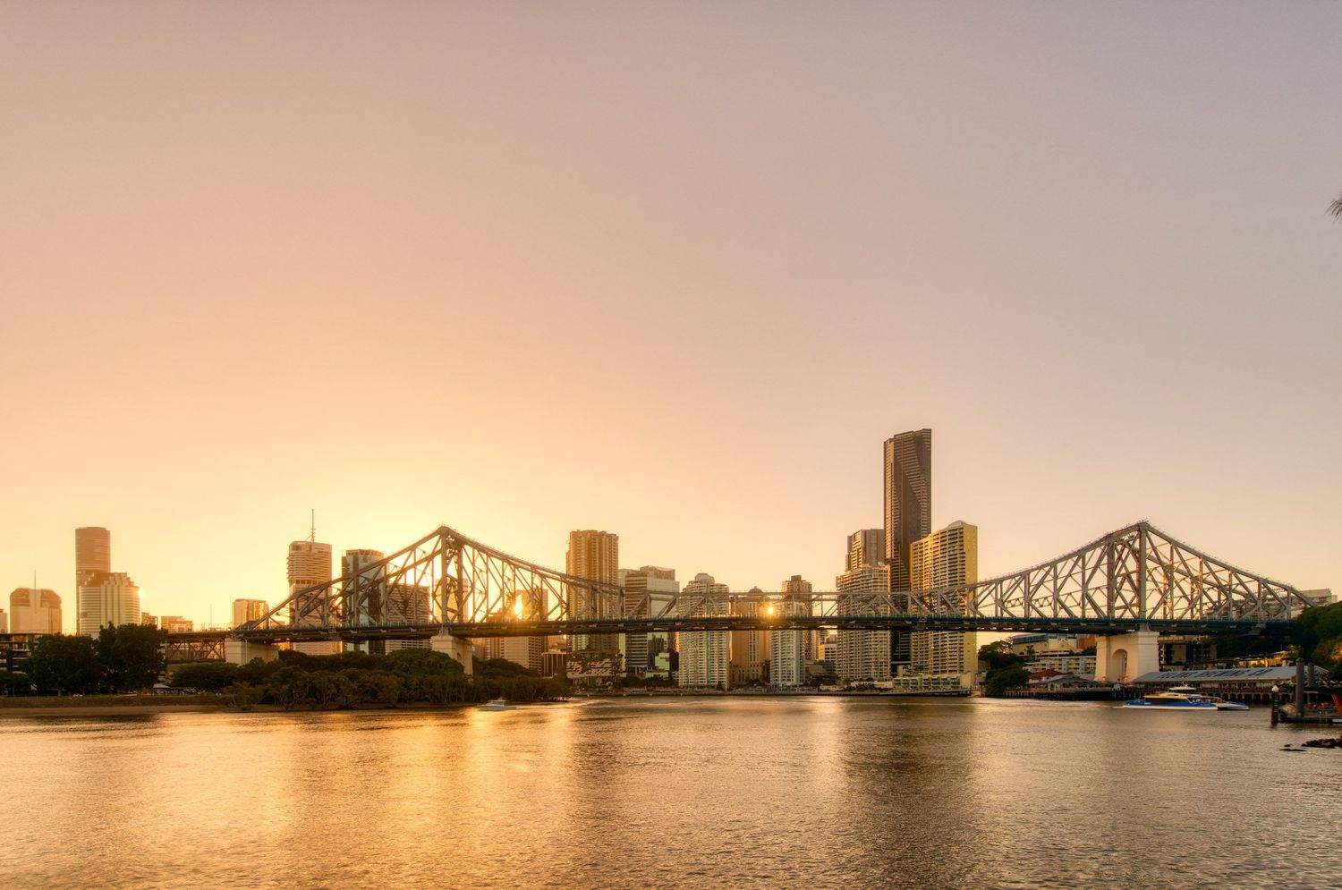 Brisbane Story Bridge and city skyline reflected in the river during a warm golden sunset.