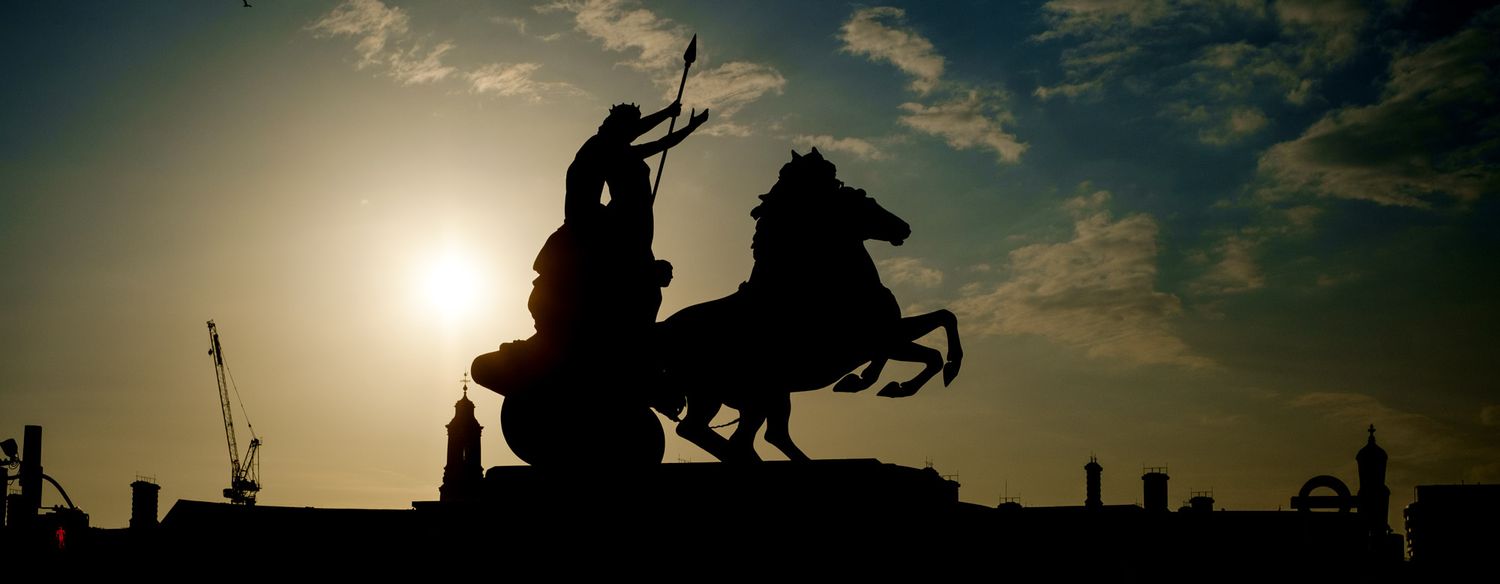 Dramatic silhouette of Boadicea chariot statue against golden sunset sky on London's Westminster Bridge.
