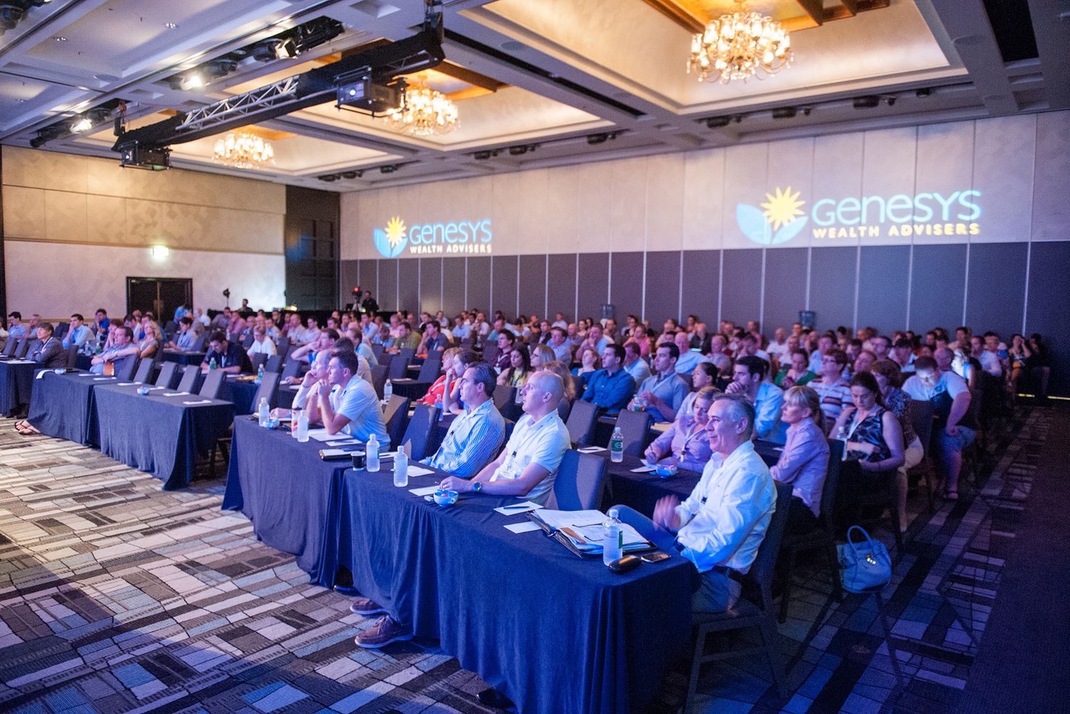 Large crowd of business professionals seated at tables during a Genesys Wealth Advisers conference.