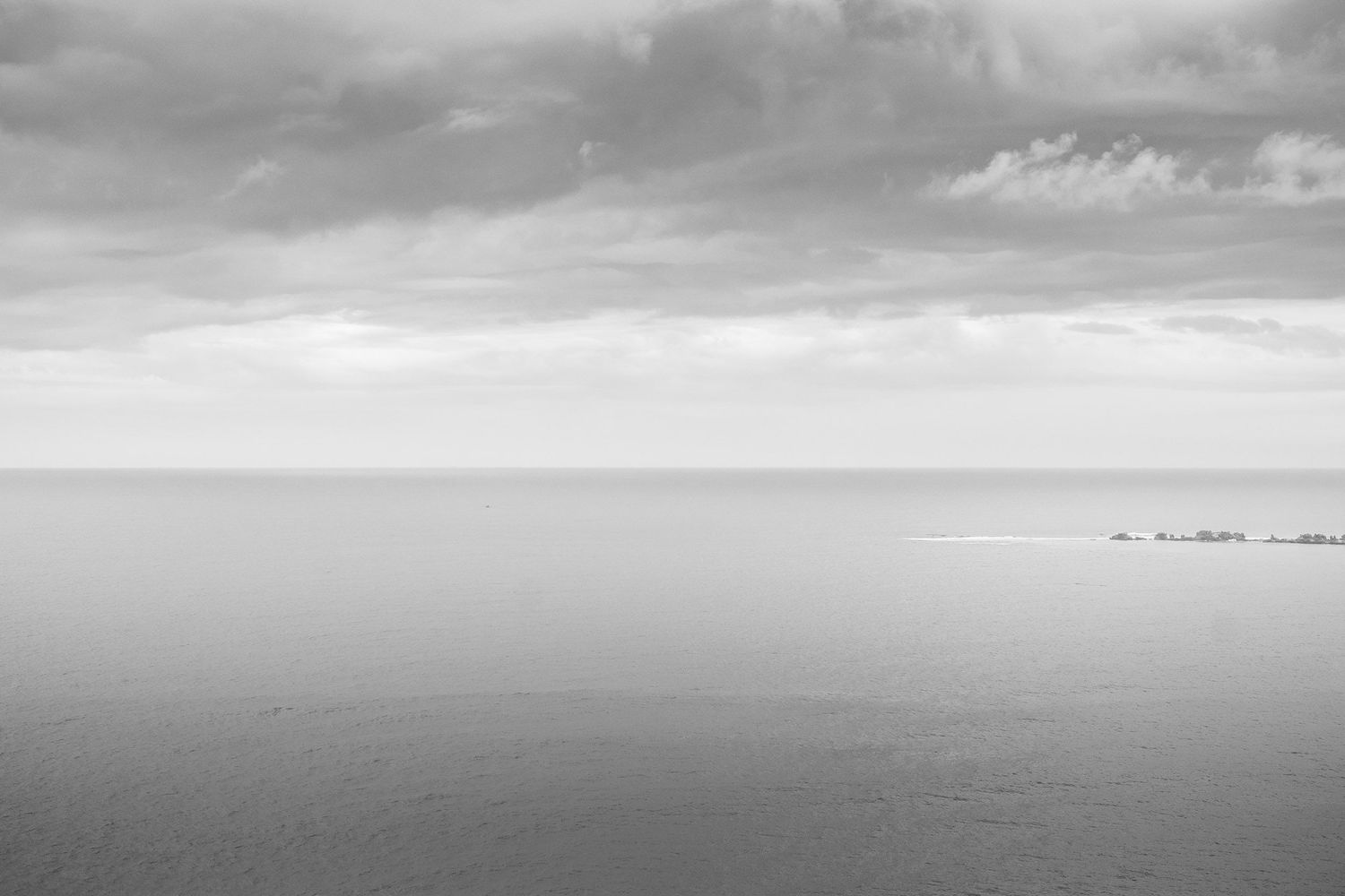 Minimalist black and white seascape with calm ocean waters under dramatic cloudy sky.