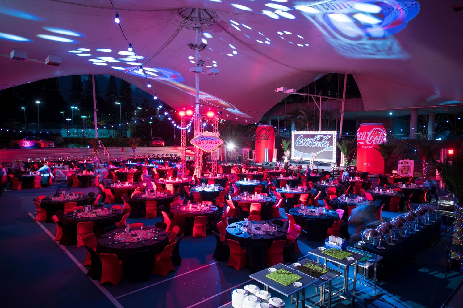 A large Coca-Cola branded gala dinner event with round tables under a white tent with red lighting.