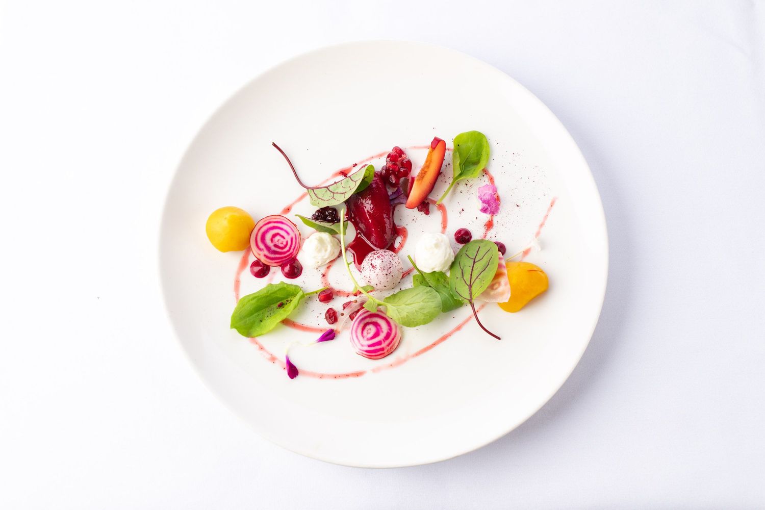 Elegant fine dining salad with colorful beets, yellow tomatoes, and microgreens on a white plate.
