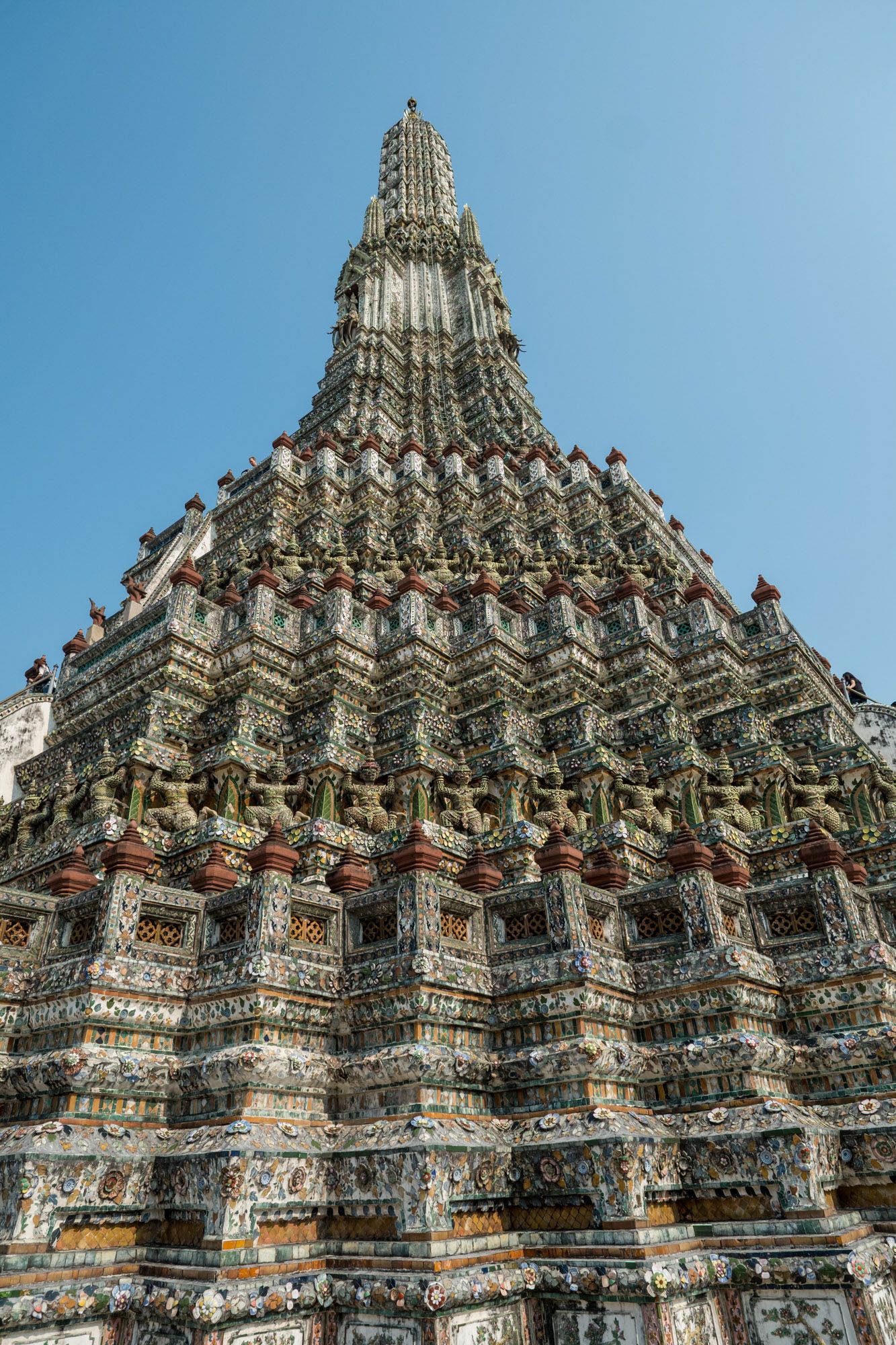 Ornate ancient Wat Arun temple spire with detailed ceramic mosaic decorations against blue sky Bangkok.