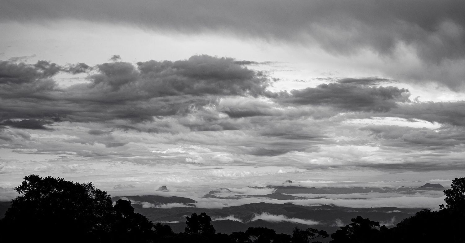 Black and white panoramic landscape of rolling hills under dramatic stormy clouds at dusk.